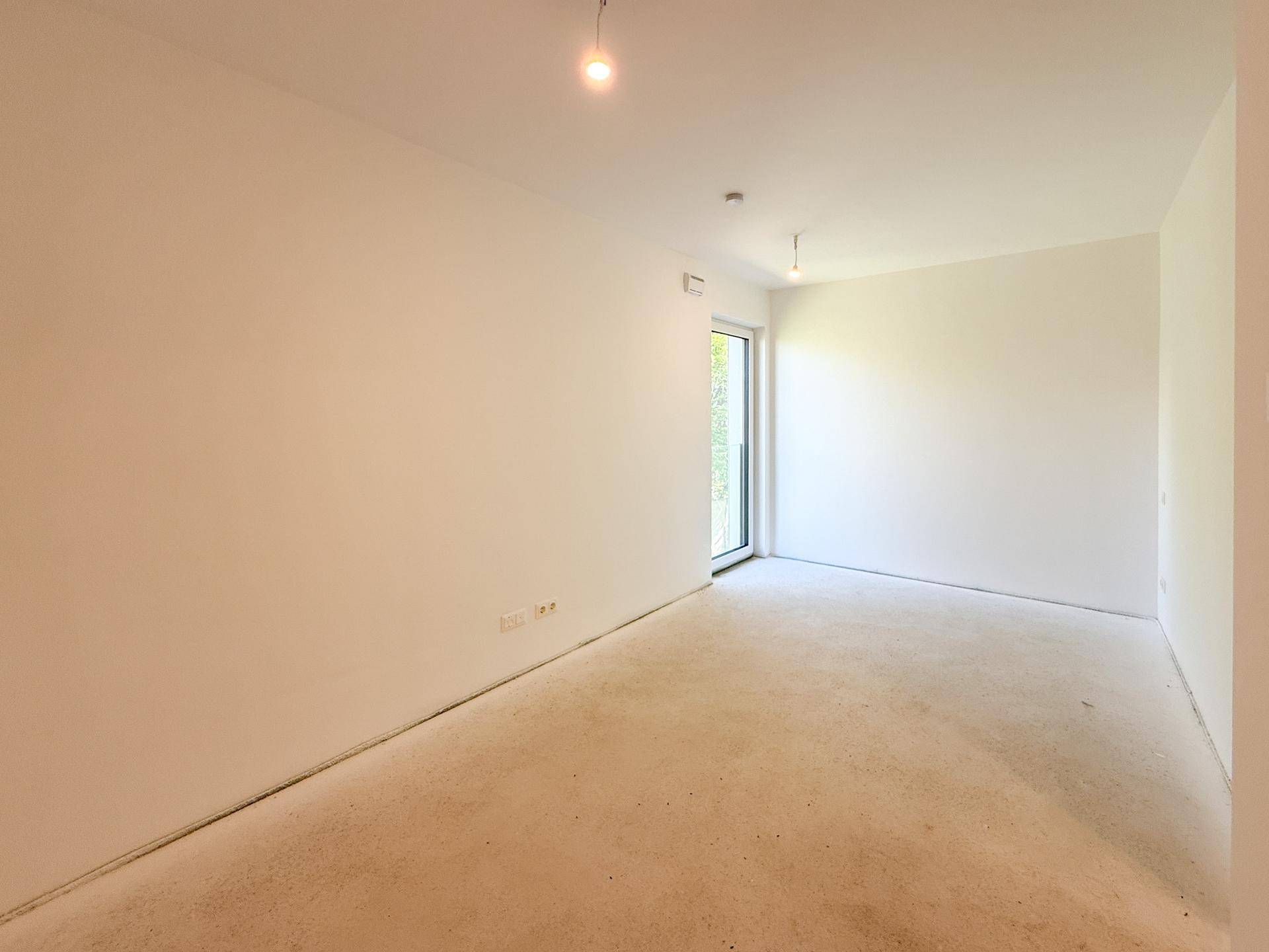 Unmöbliertes Schlafzimmer im Rohbau mit Fenster und viel Tageslicht.