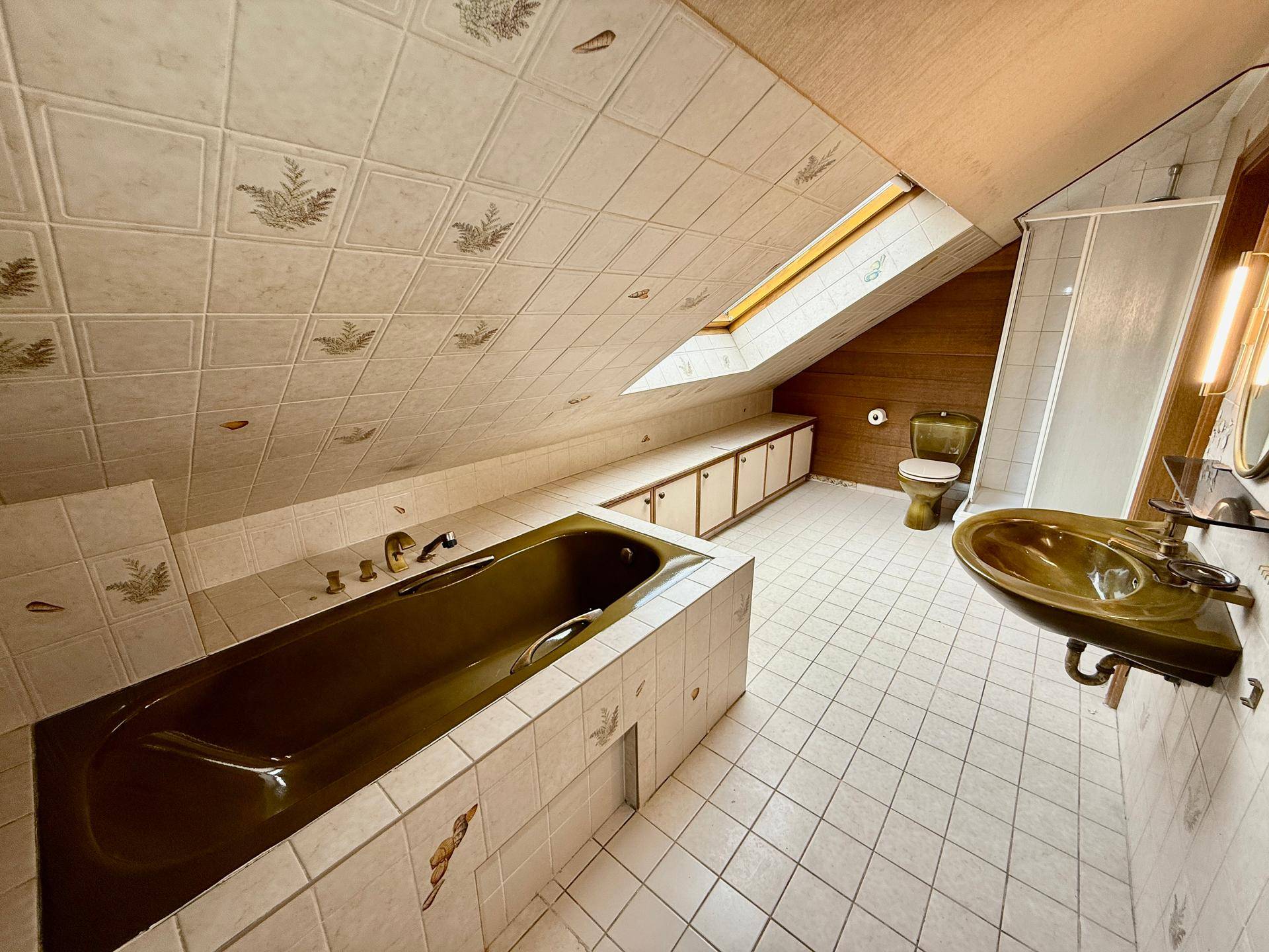 Badezimmer im Dachgeschoss mit Badewanne, Dachfenster und Fliesen im 80er-Jahre-Stil.