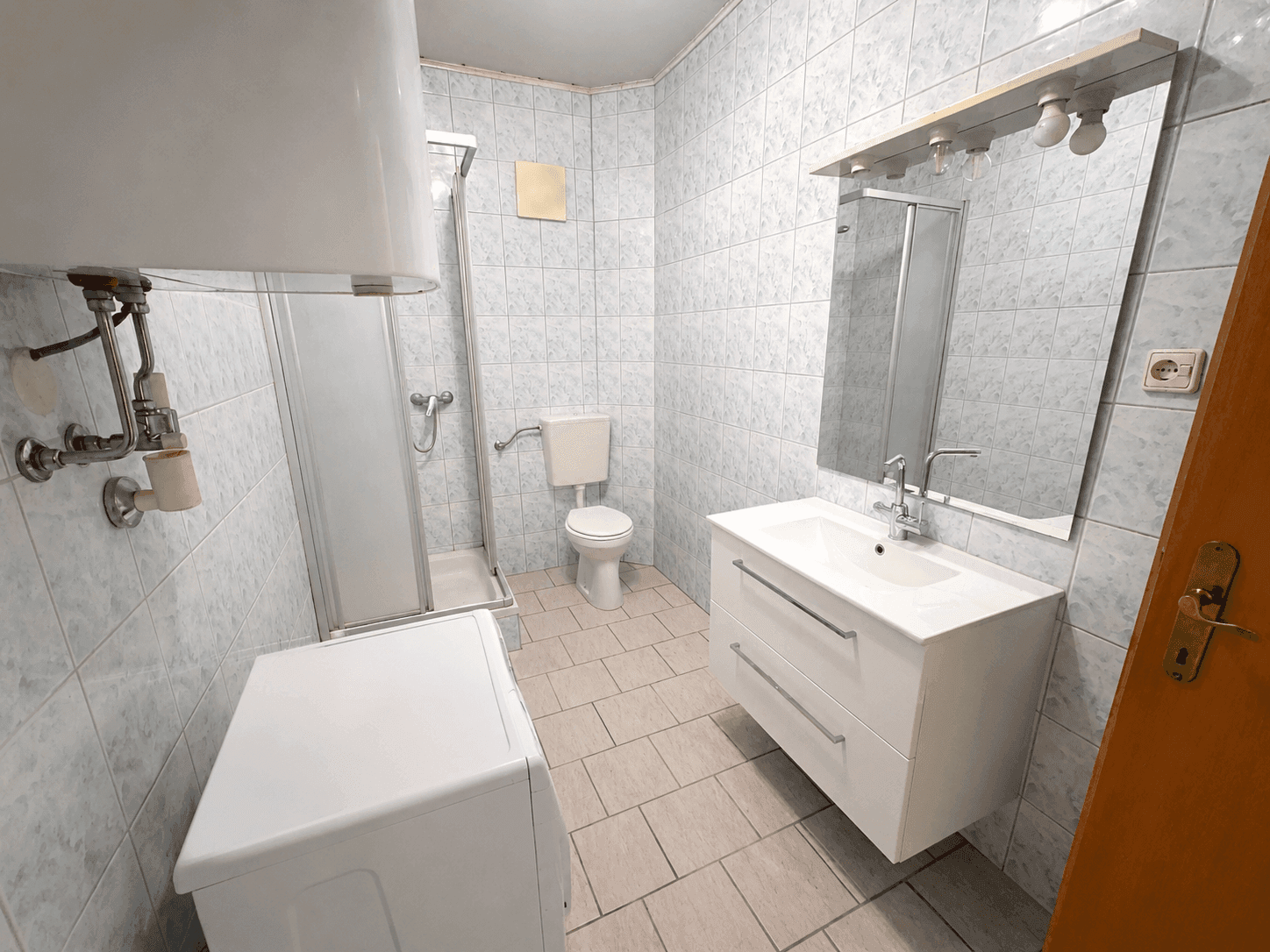 Gefliestes Badezimmer mit Dusche, Waschbecken, Toilette und Waschmaschine.