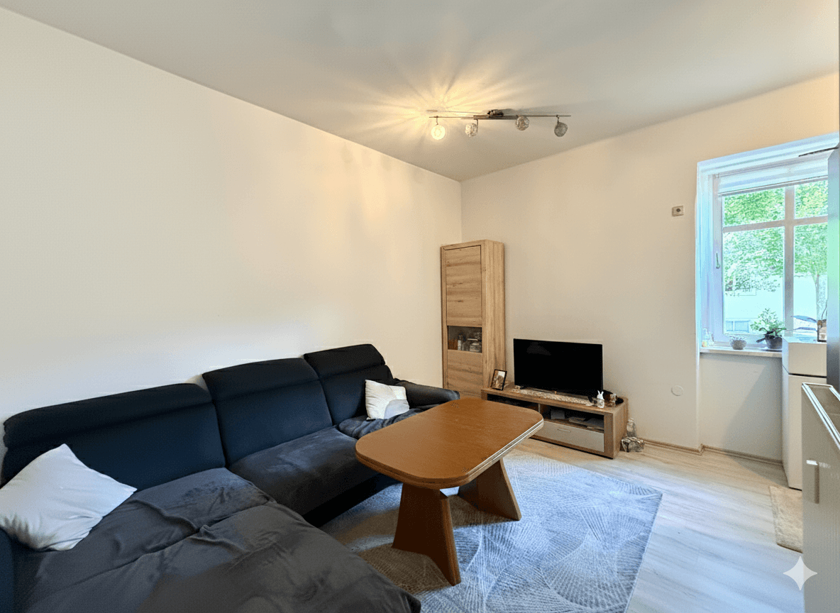 Helles Wohnzimmer mit bequemer Couch, TV-Möbel und Laminatboden, gut beleuchtet durch ein Fenster.