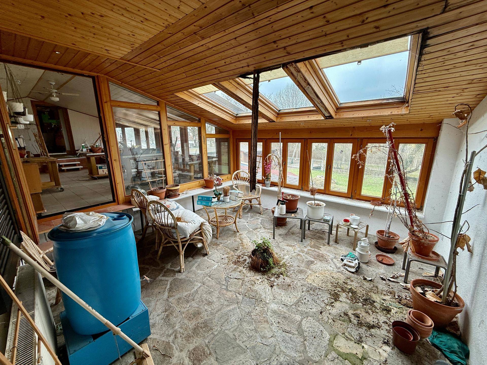 Geräumiger Wintergarten mit Steinboden, vielen Fenstern und Oberlichtern, ideal für Pflanzen.