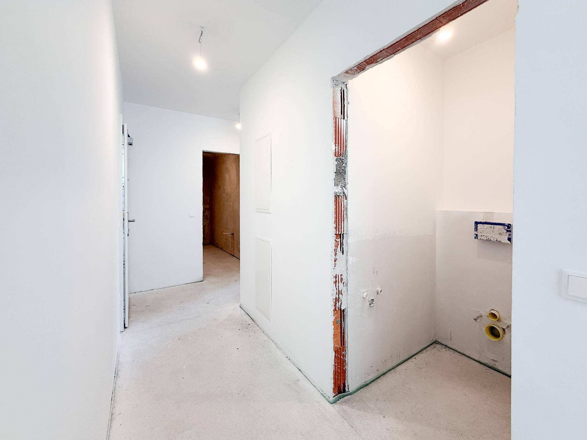 Heller Flur im Rohbau mit Zugang zu weiteren Räumen und einem Badezimmer im Bau.
