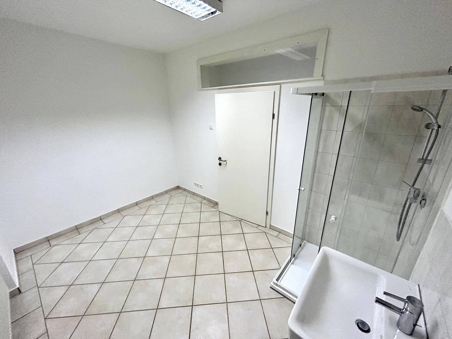 Einfaches Badezimmer mit Duschkabine, Waschbecken und Fliesenboden.