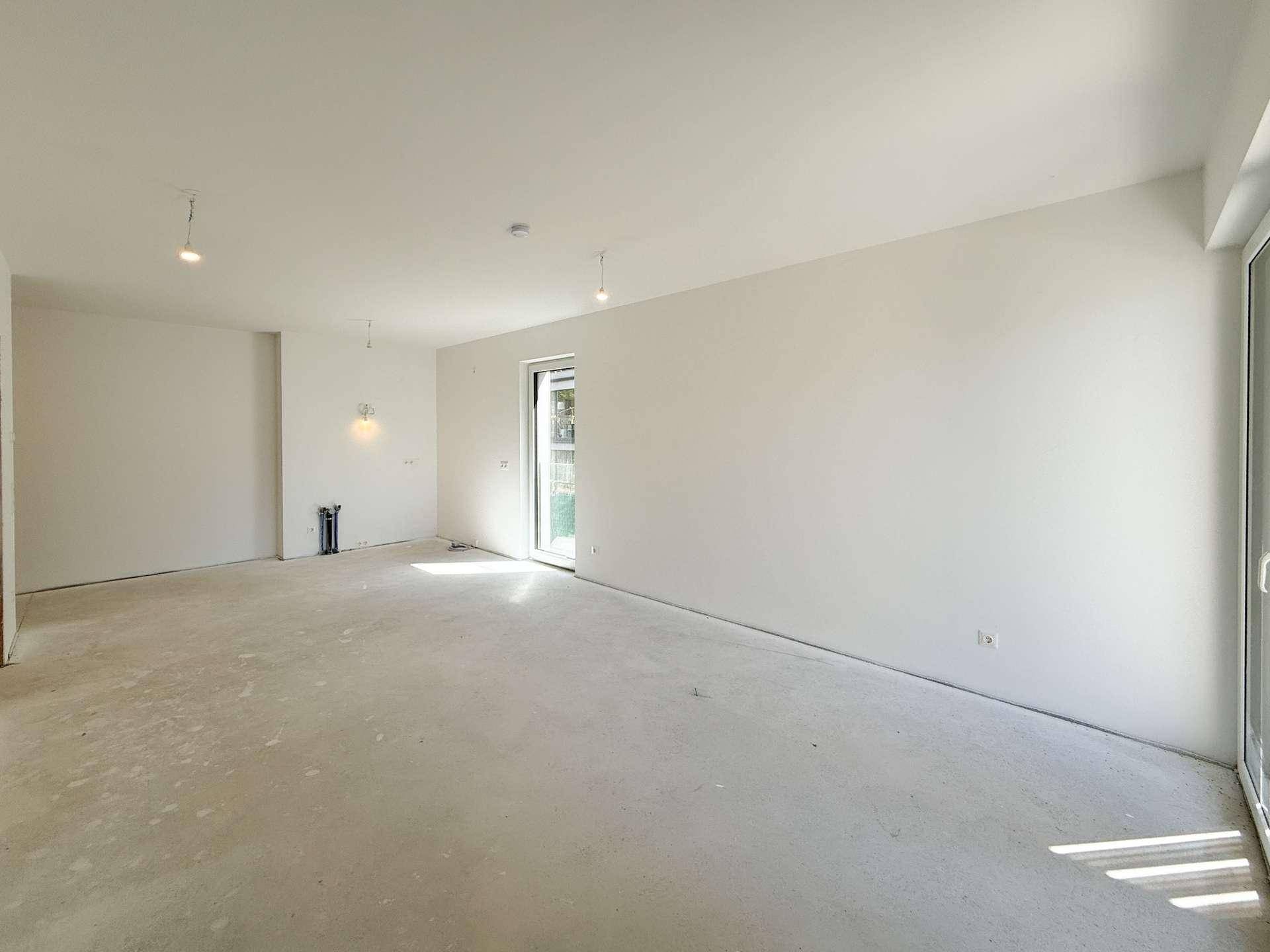 Geräumiger, unmöblierter Raum im Rohbau mit großem Fenster, bereit für den Innenausbau.
