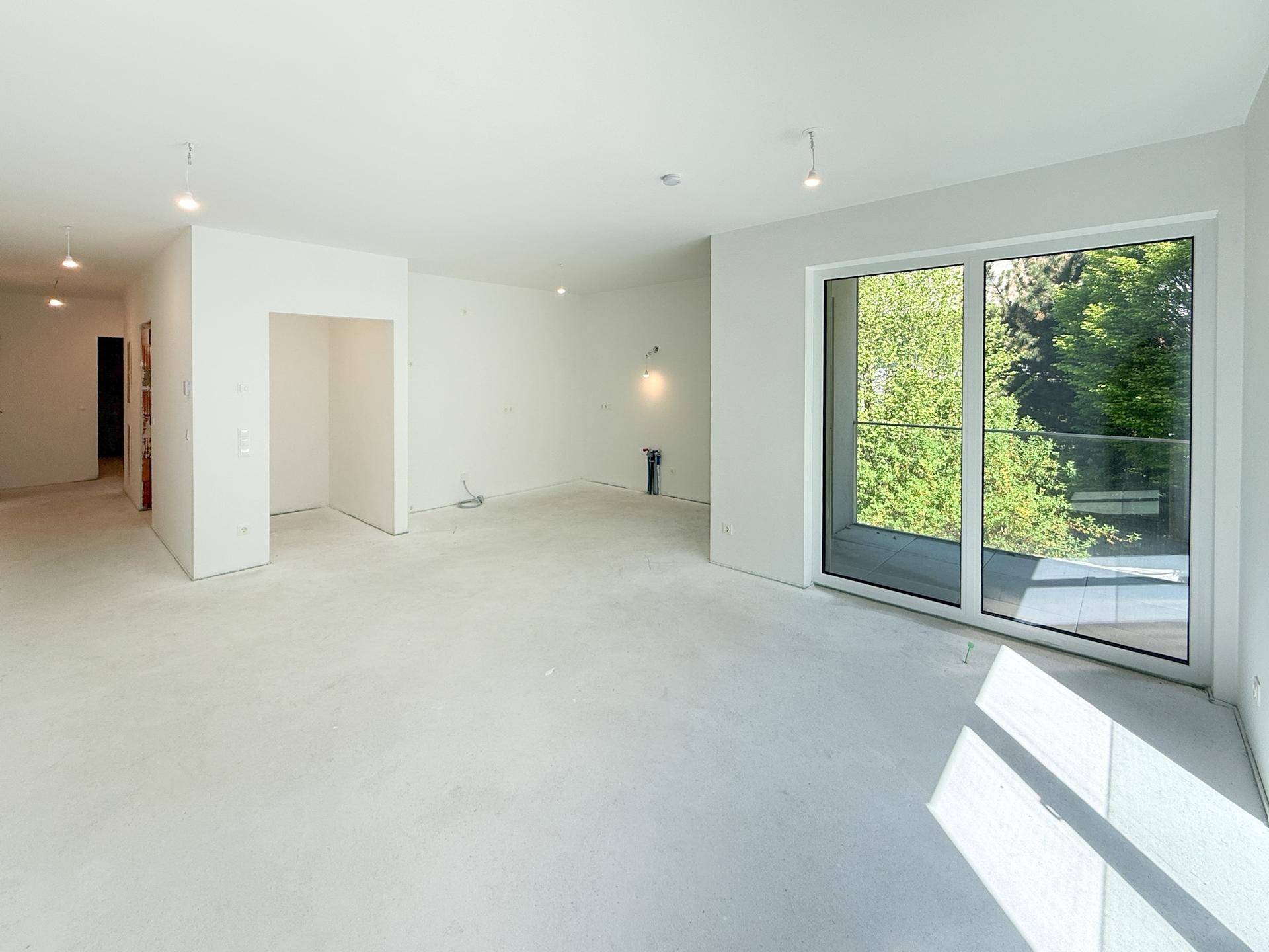 Unmöblierter Raum im Neubau mit breiter Fensterfront und Blick ins Grüne.