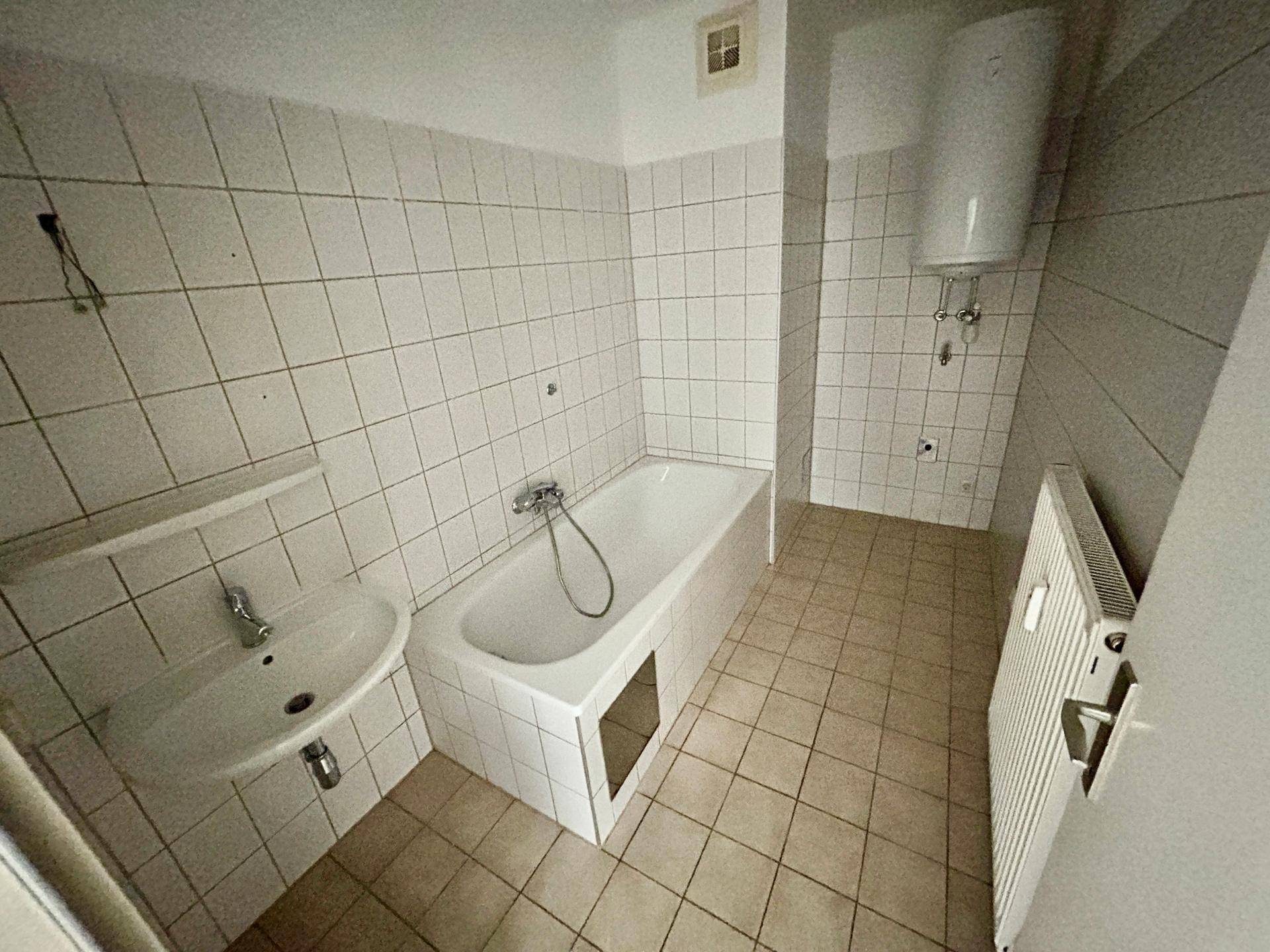 Badezimmer mit Badewanne, Waschbecken und Boiler, komplett gefliest in einem älteren Stil.