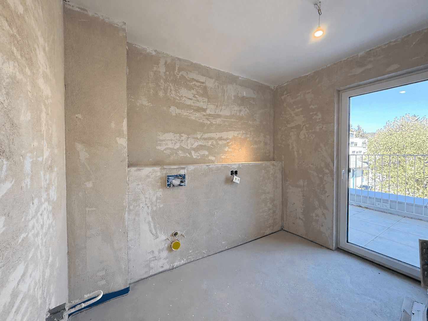 Rohbauraum mit sichtbaren Installationen und Zugang zu einem Außenbereich, bereit für den Ausbau.