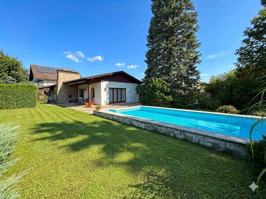 Gesamtansicht des Hauses mit großem Garten und langem Swimmingpool unter blauem Himmel.