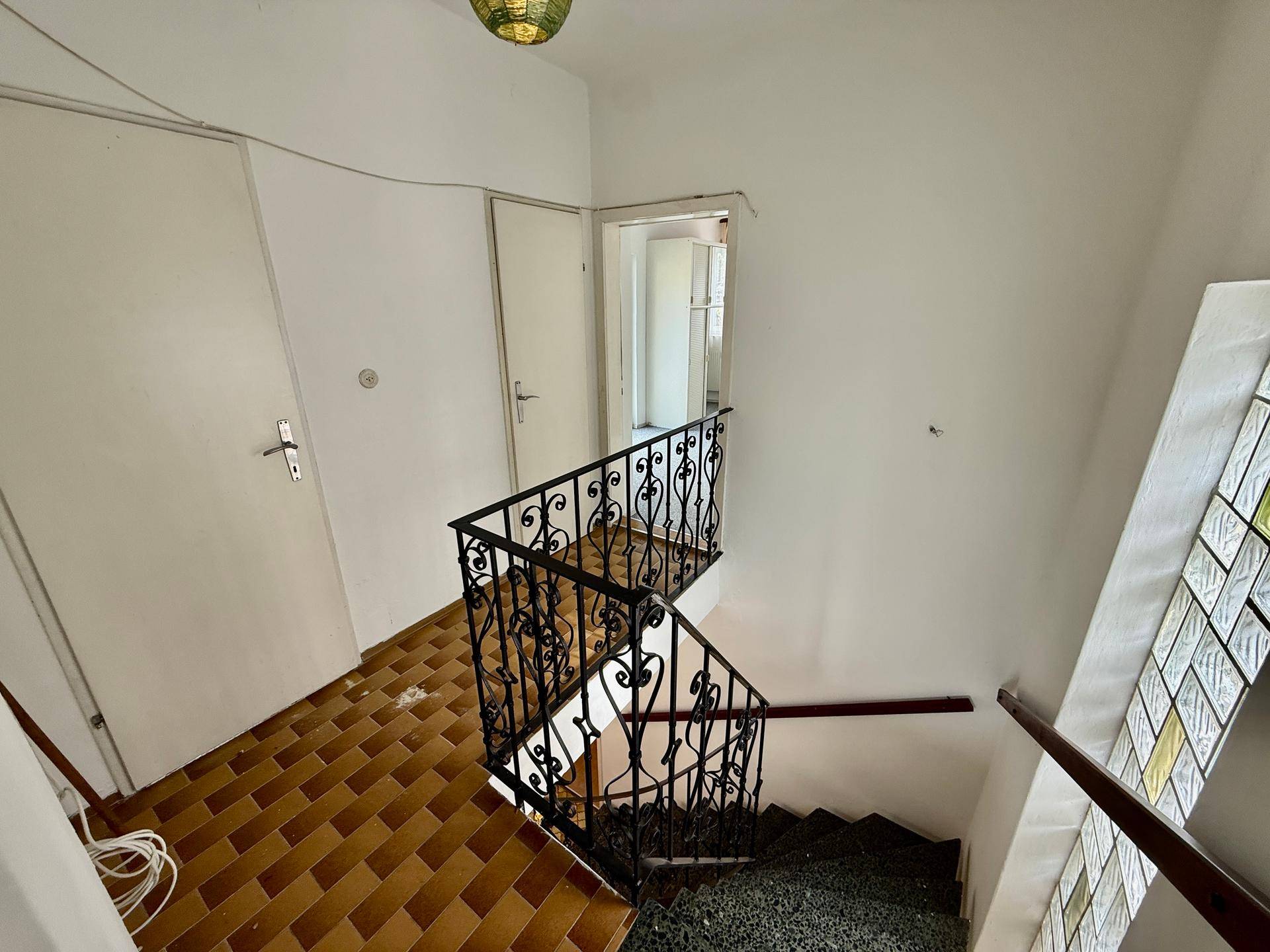 Treppenhaus mit schmiedeeisernem Geländer und gefliestem Boden.