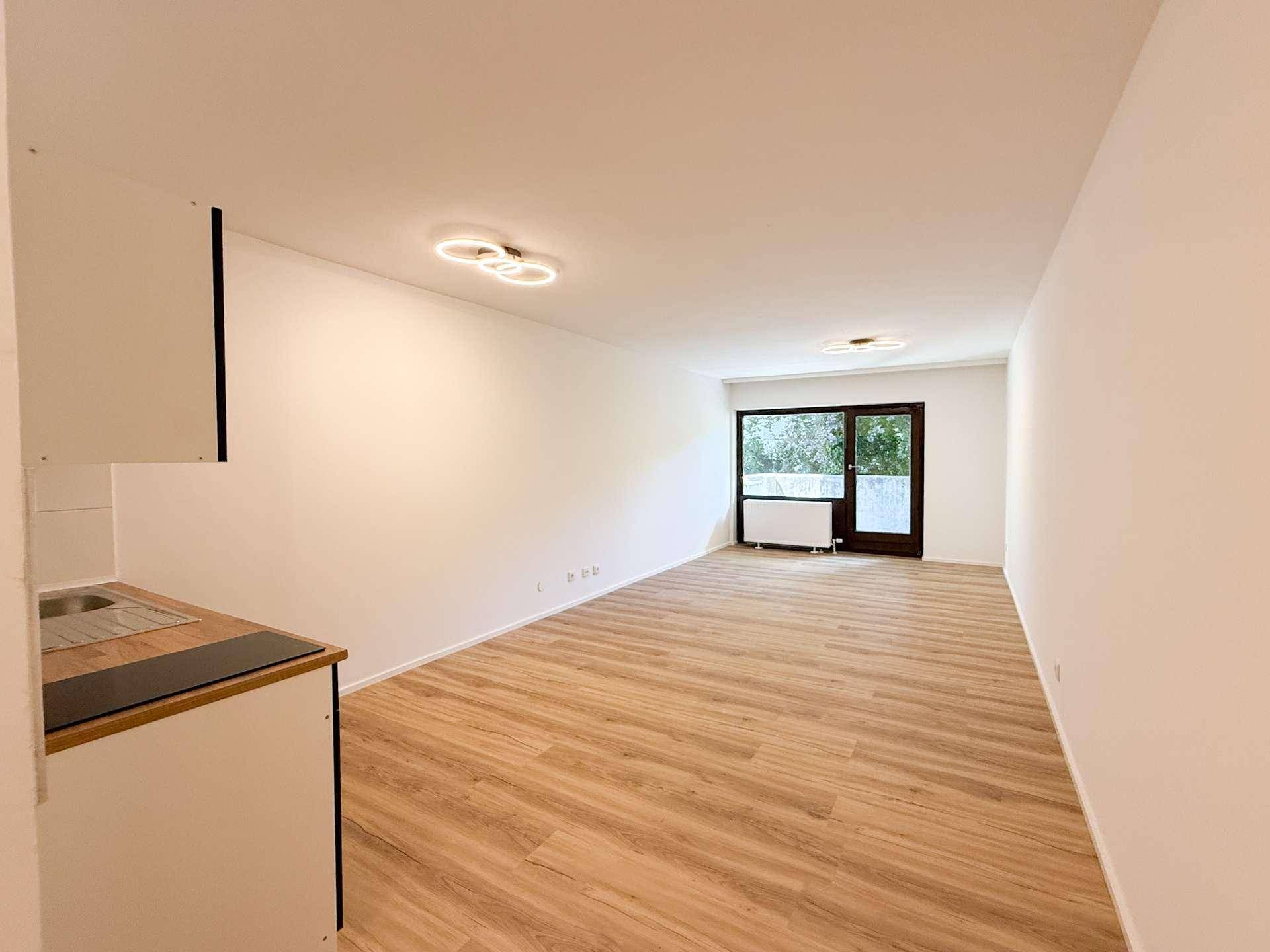 Geräumiger Wohnbereich mit Laminatboden und Zugang zu einem Außenbereich durch eine große Glastür.