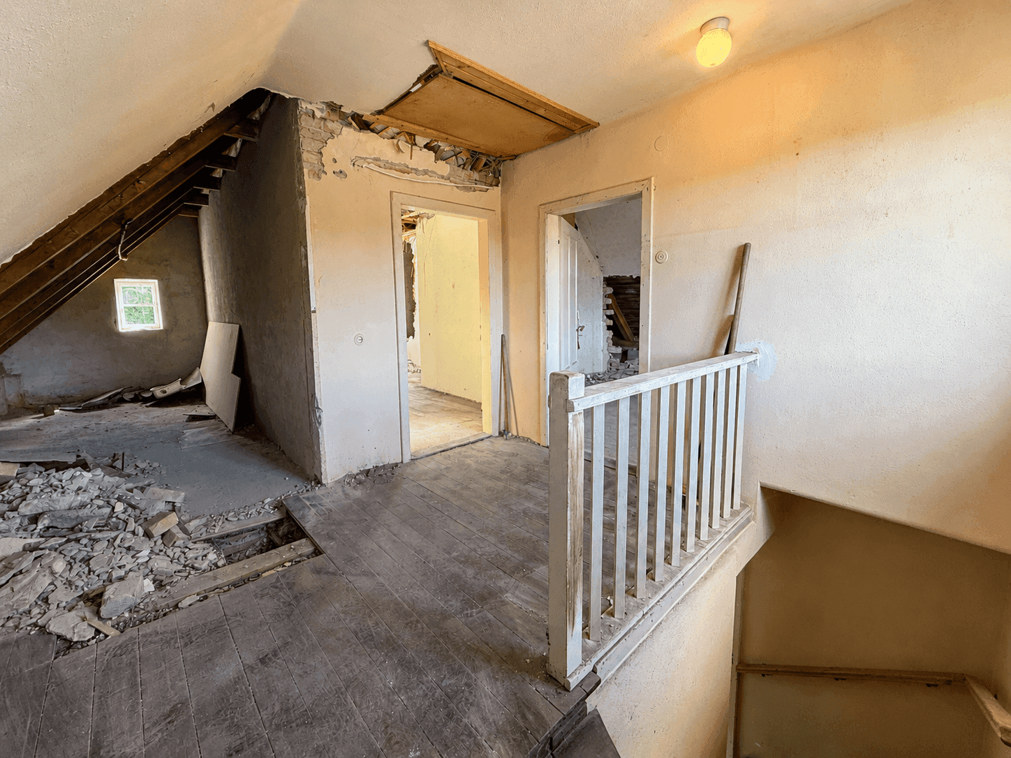 Dachgeschoss im Rohbau mit sichtbaren Dachbalken, Schutt und Treppengeländer.