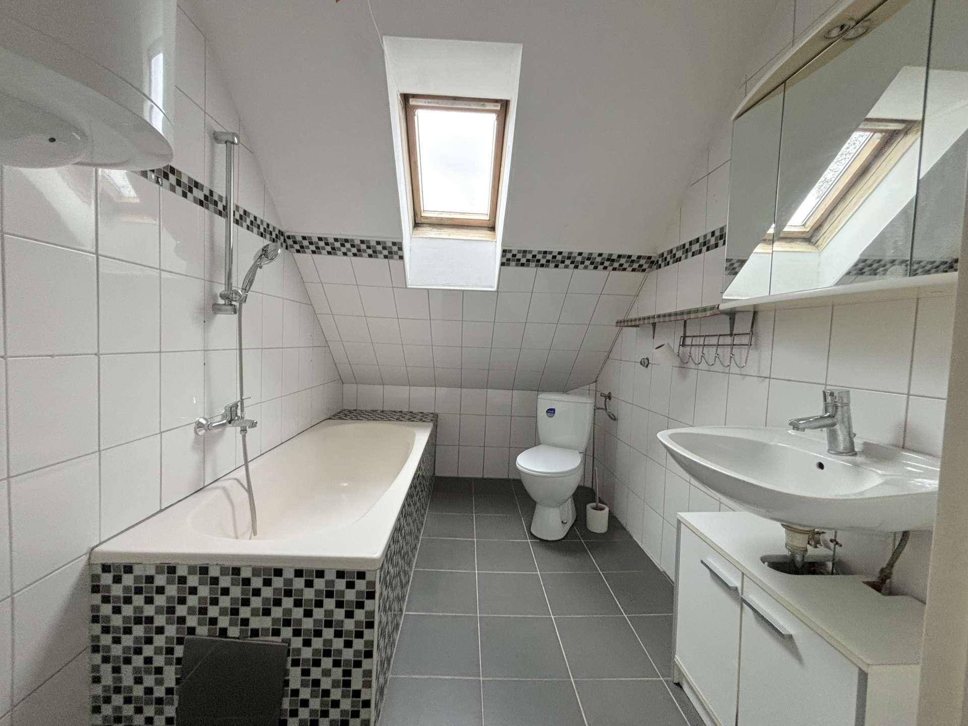 Badezimmer mit Badewanne, WC und Dachfenster, hell gefliest.