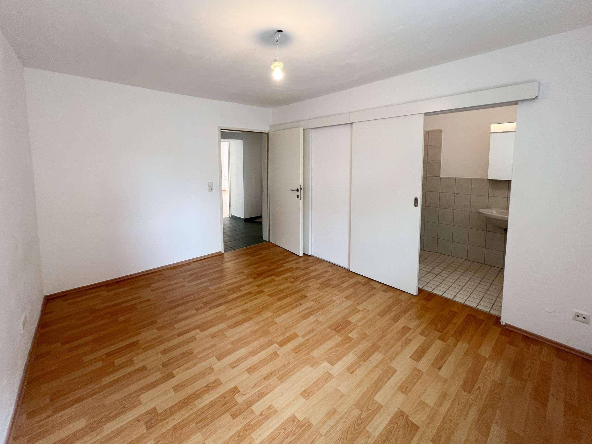 Schlafzimmer mit Laminatboden und Zugang zu Bad und Ankleidebereich.