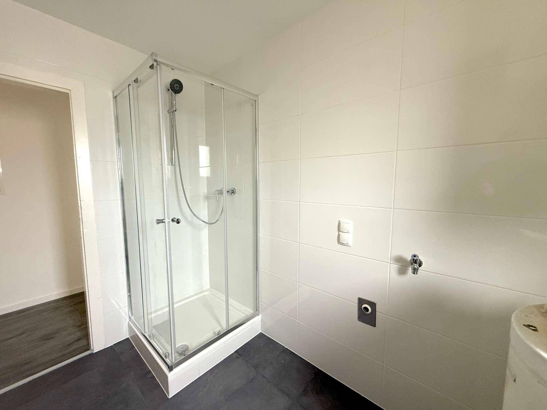 Modernes Badezimmer mit weiß gefliesten Wänden und einer Eckduschkabine, bereit zur Nutzung.