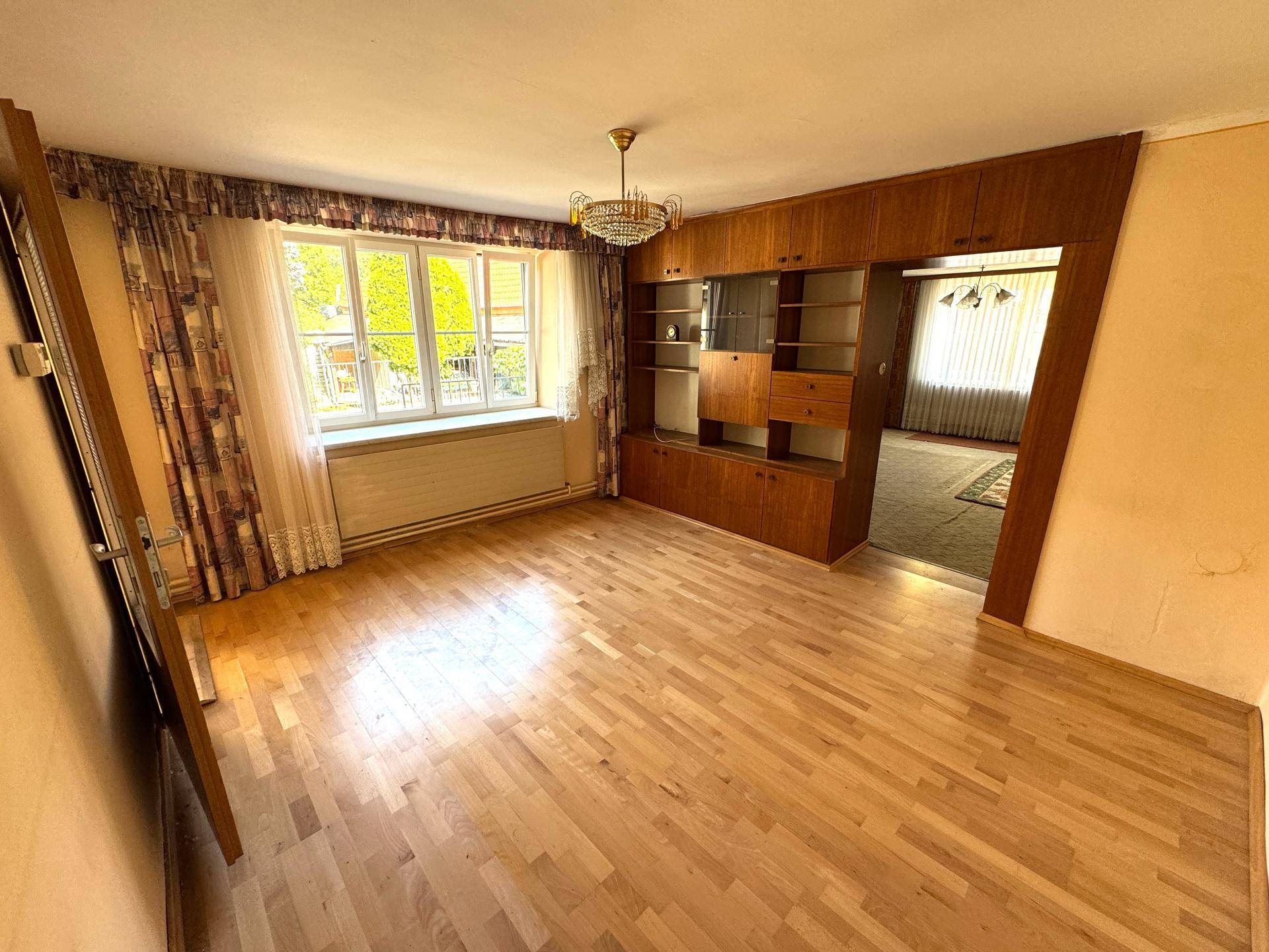 Geräumiges Wohnzimmer mit Holzparkett, Einbauschränken und Blick ins Grüne.
