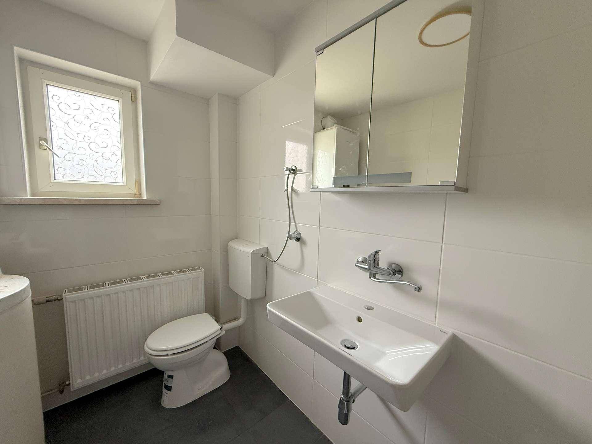 Funktionales Badezimmer mit WC, Waschbecken, Spiegelschrank und einem Fenster für natürliches Licht.