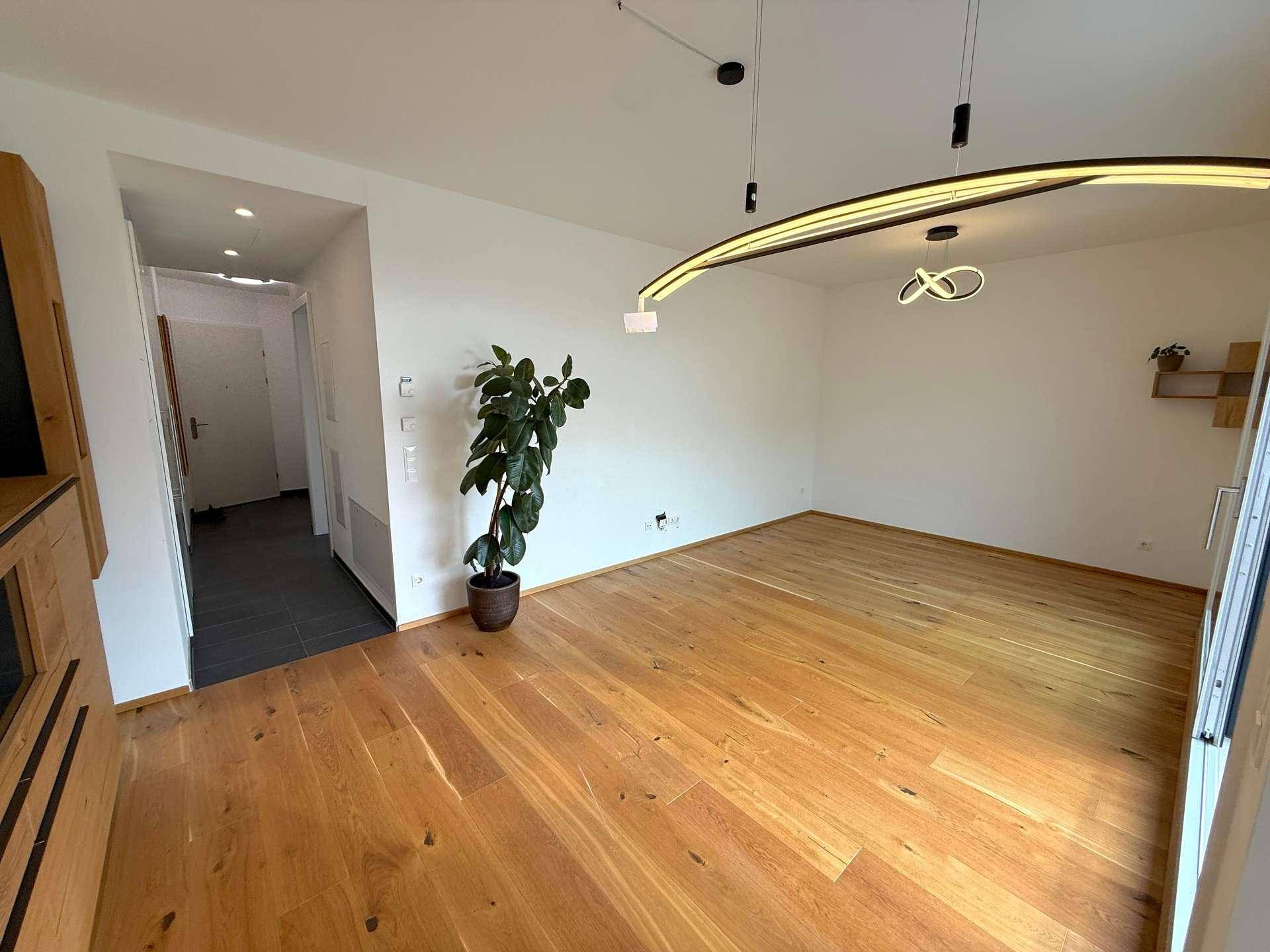 Geräumiges Wohnzimmer mit hellem Holzboden, weißen Wänden und moderner Deckenbeleuchtung.
