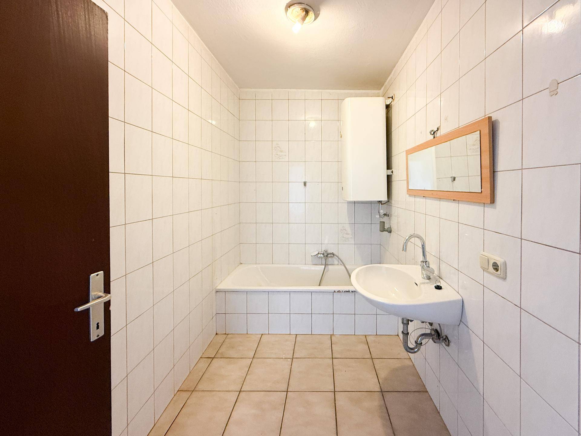 Badezimmer mit weißen Fliesen, Badewanne und Waschbecken, das eine funktionale Ausstattung bietet.