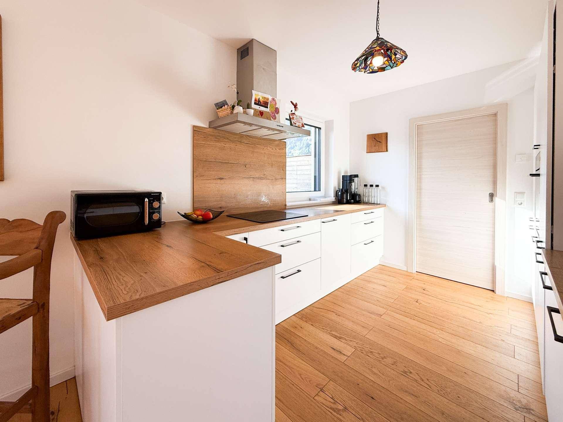 Funktionale Küche mit weißen Unterschränken, Holz-Arbeitsplatte und Mikrowelle.