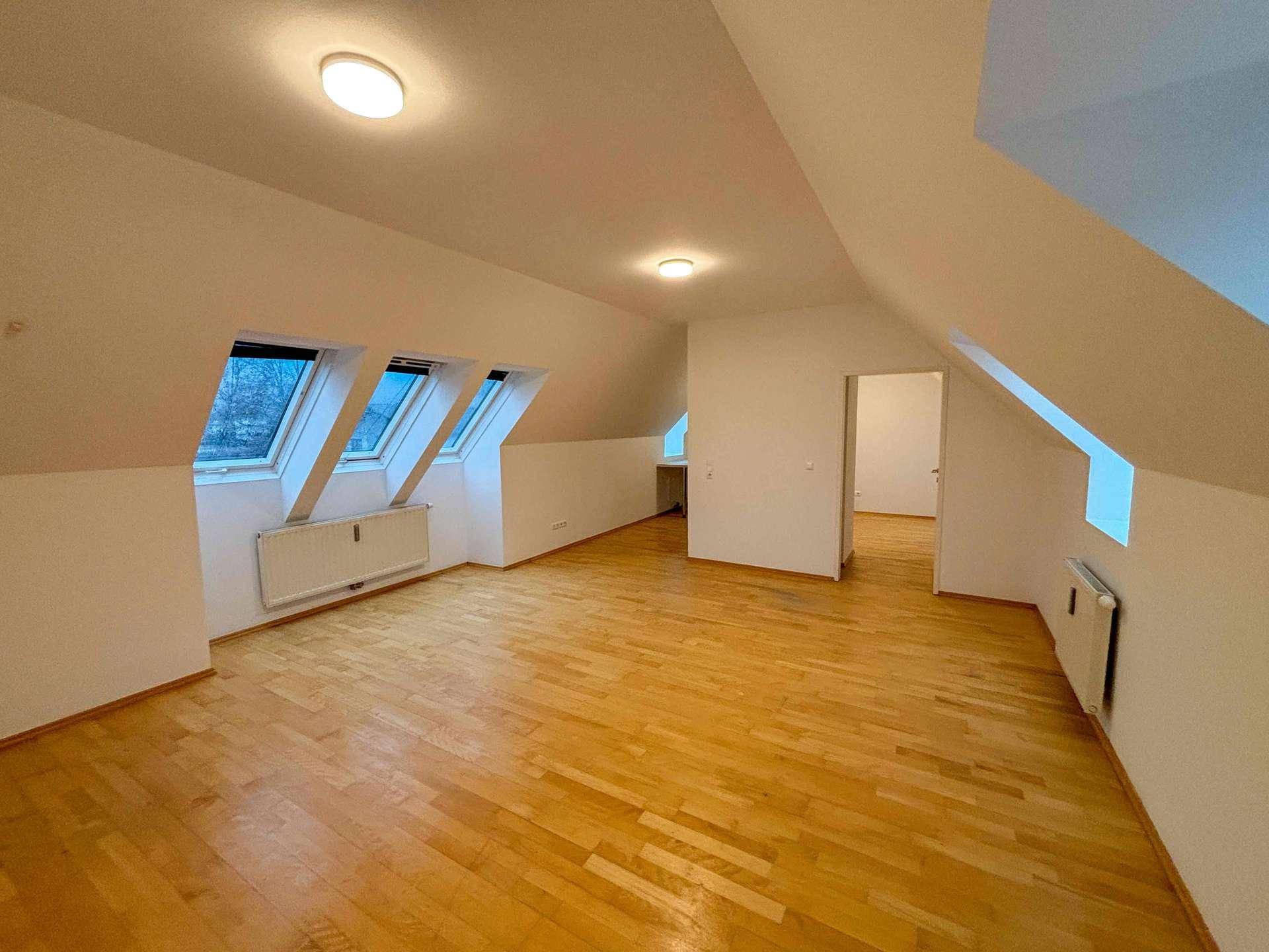 Geräumiger Dachgeschossraum mit Holzboden, Dachfenstern und Zugang zu weiteren Zimmern.