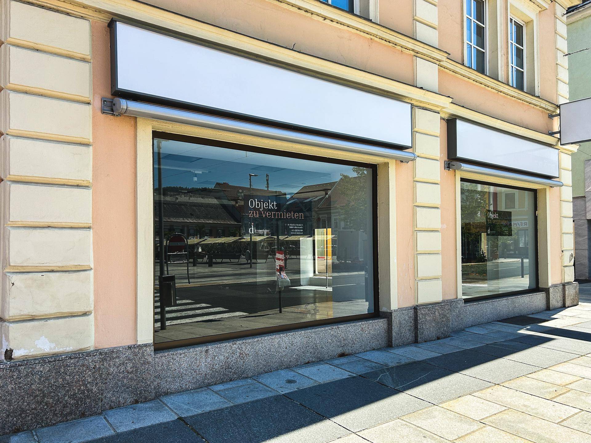 Nahaufnahme der Ladenfront mit zwei großen Schaufenstern und 'Objekt zu vermieten'-Schildern.