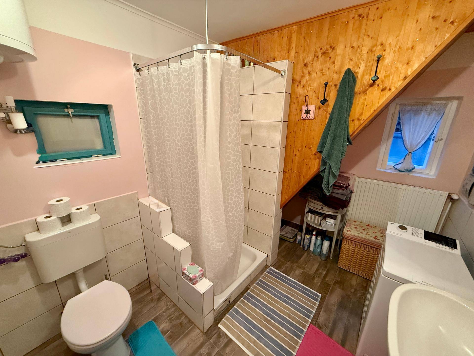 Badezimmer mit Dusche, WC, Waschbecken und Waschmaschine unter einer Holzschräge.