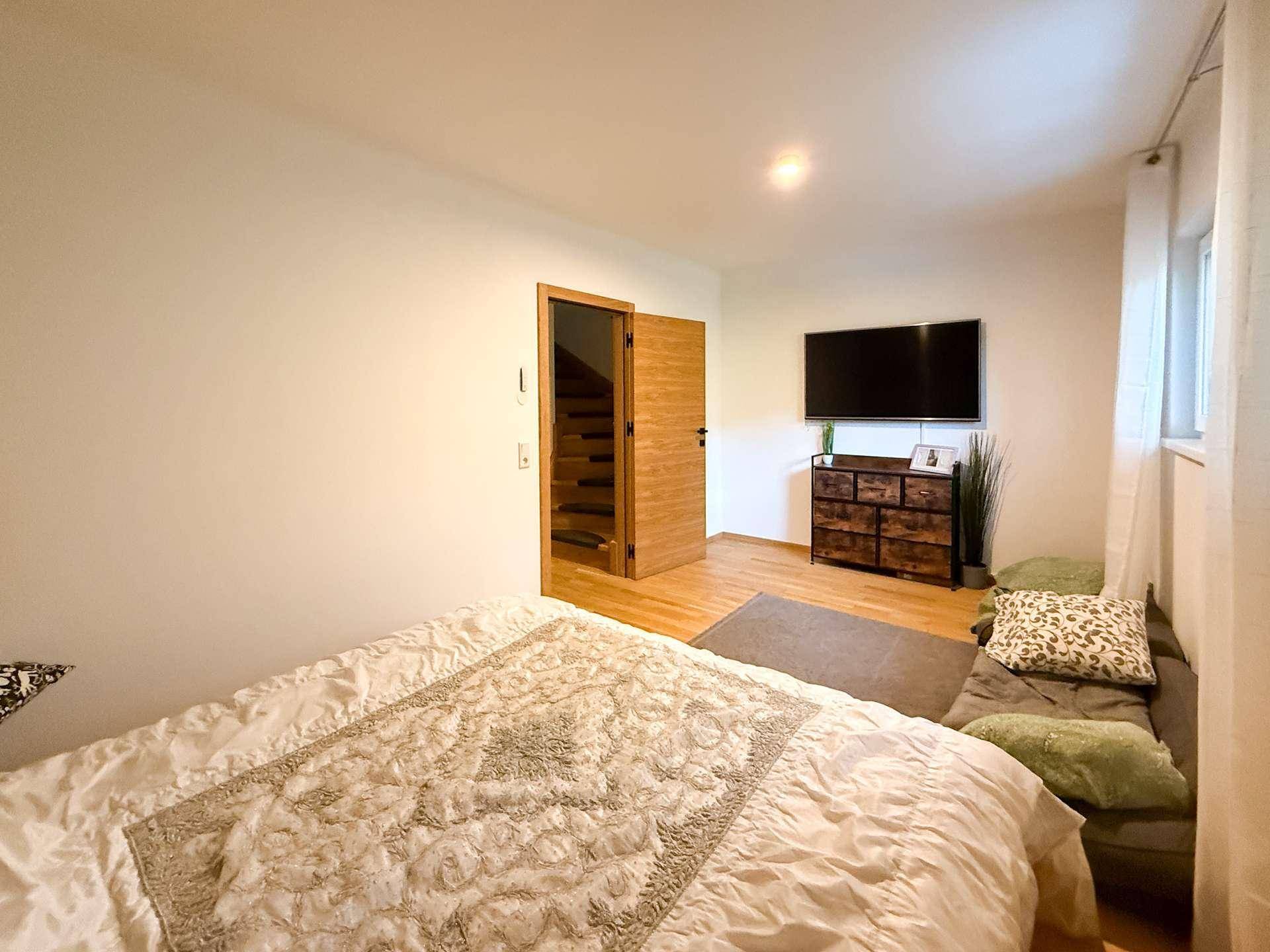 Gemütliches Schlafzimmer mit Holzboden, Fernseher und Zugang zu einer Treppe.