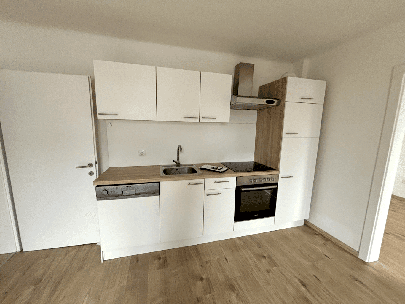 Moderne Küchenzeile mit weißen Schränken, Holz-Arbeitsplatte und integrierten Geräten.