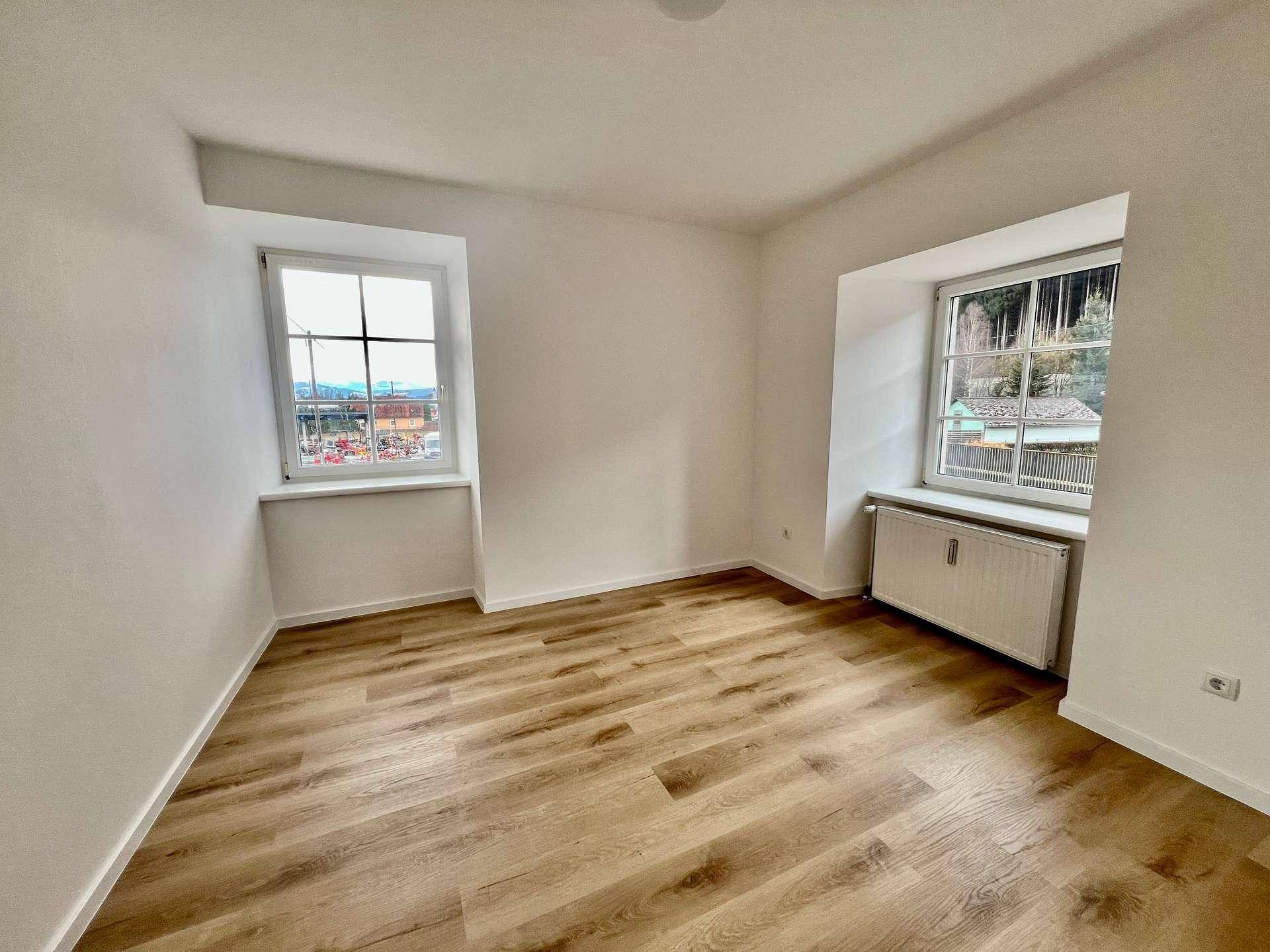 Geräumiges Zimmer mit zwei Fenstern, Laminatboden und Blick ins Grüne.