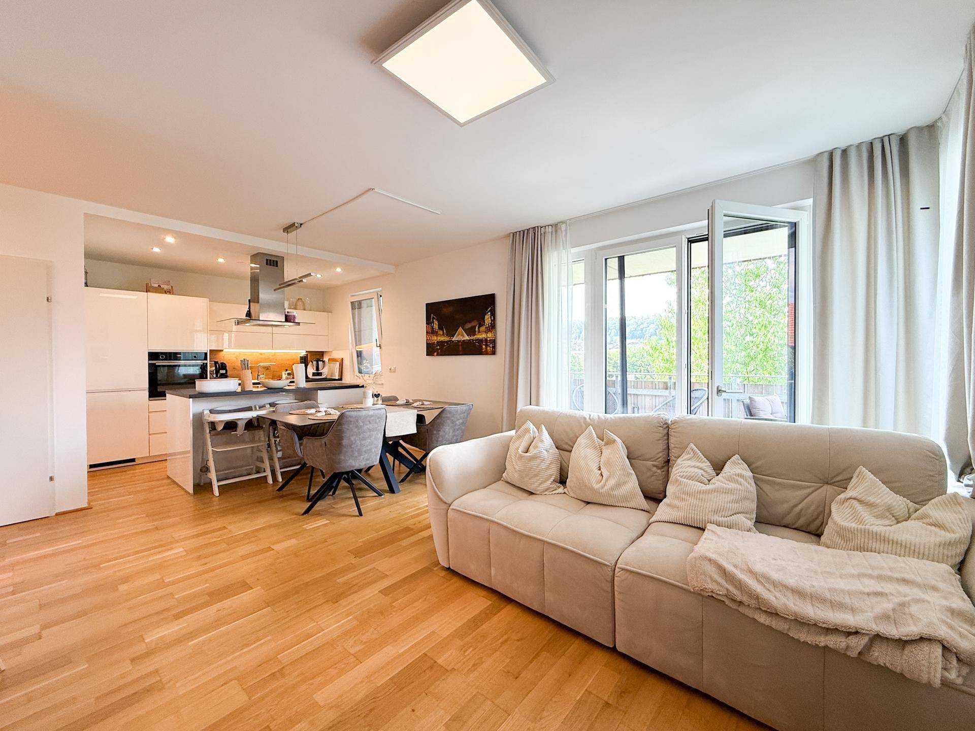 Offener Wohnbereich mit beigem Sofa, Holzboden und Blick auf die moderne Küche.