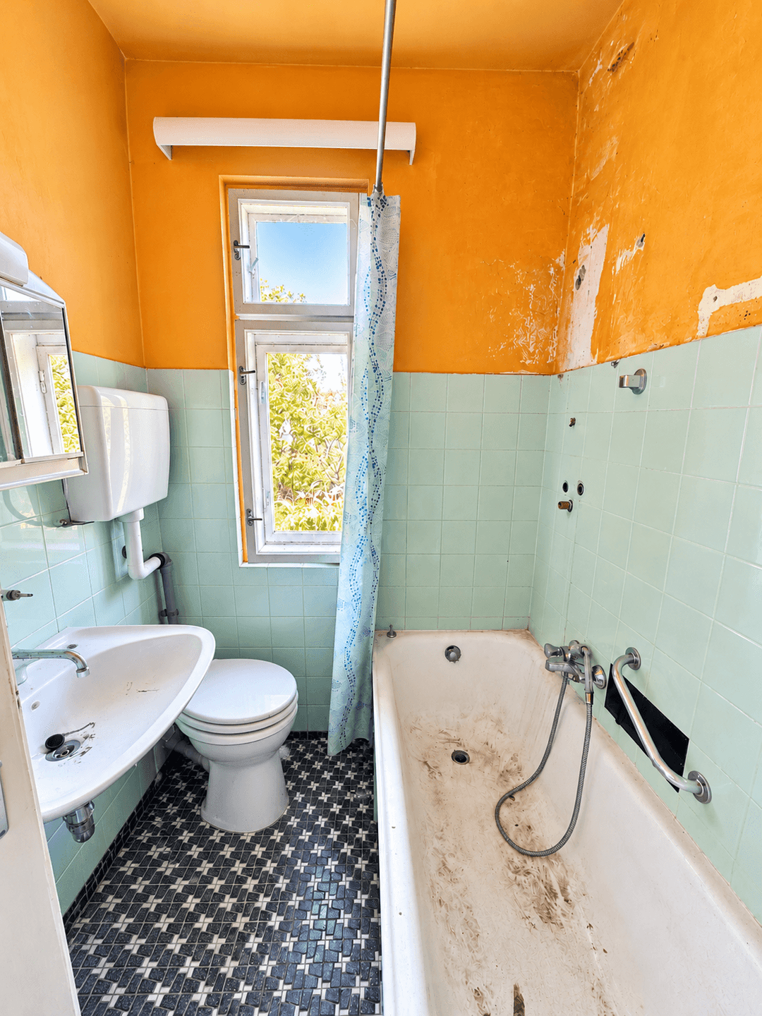 Renovierungsbedürftiges Badezimmer mit orangefarbenen Wänden, blauen Fliesen und Badewanne.