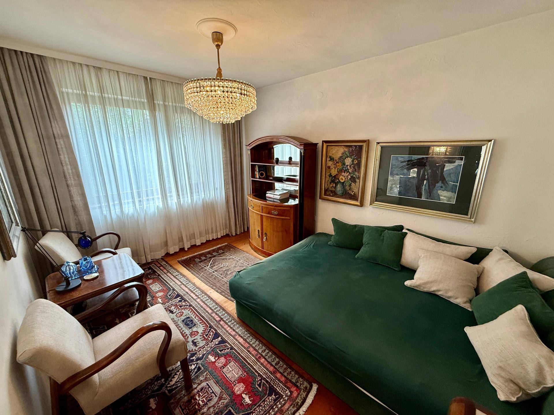 Helles Schlafzimmer mit grünem Tagesbett, Kronleuchter und traditionellem Teppichboden.