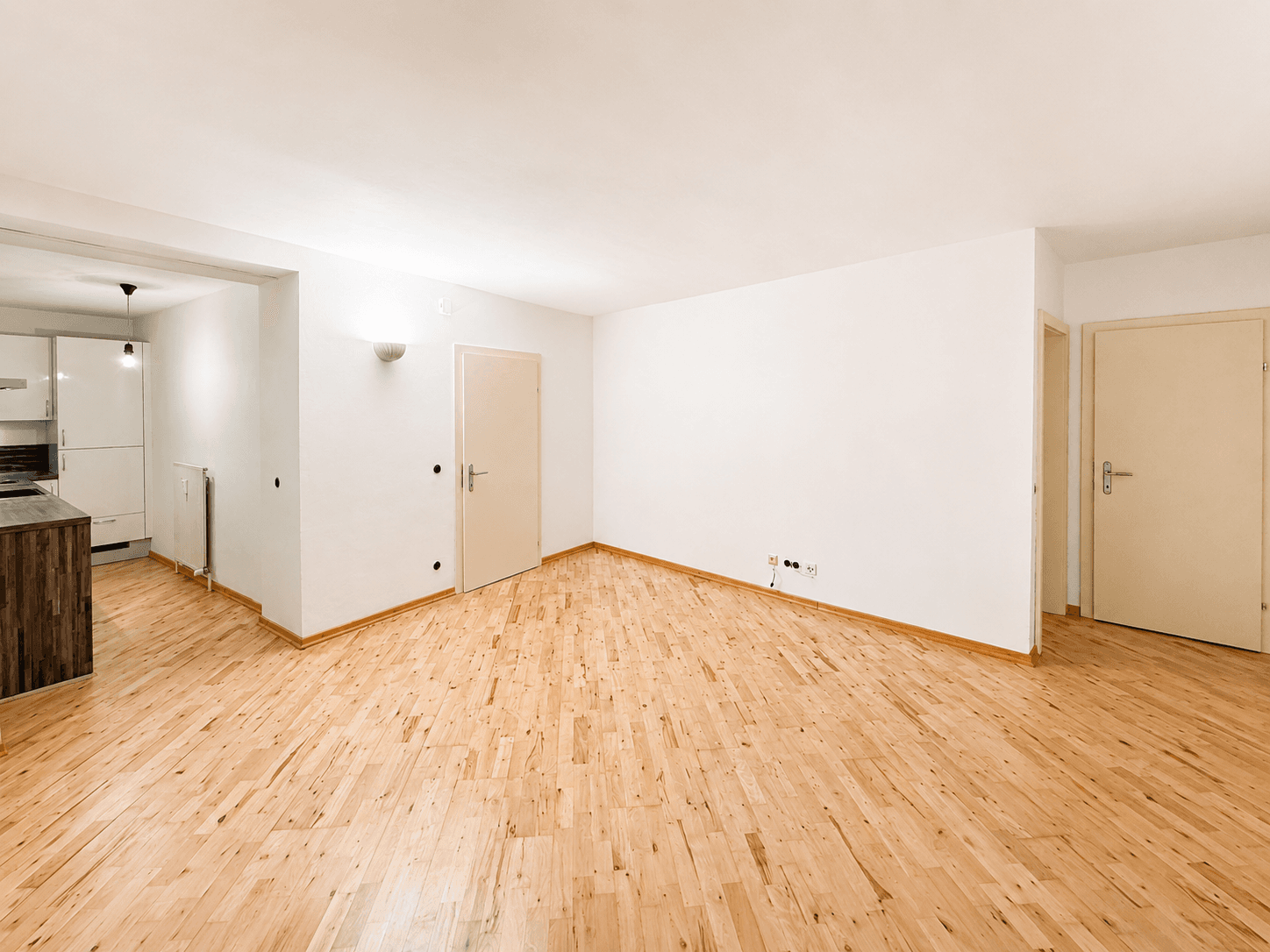 Geräumiger Wohnbereich mit hellem Holzboden und Zugang zu Küche und weiteren Räumen.