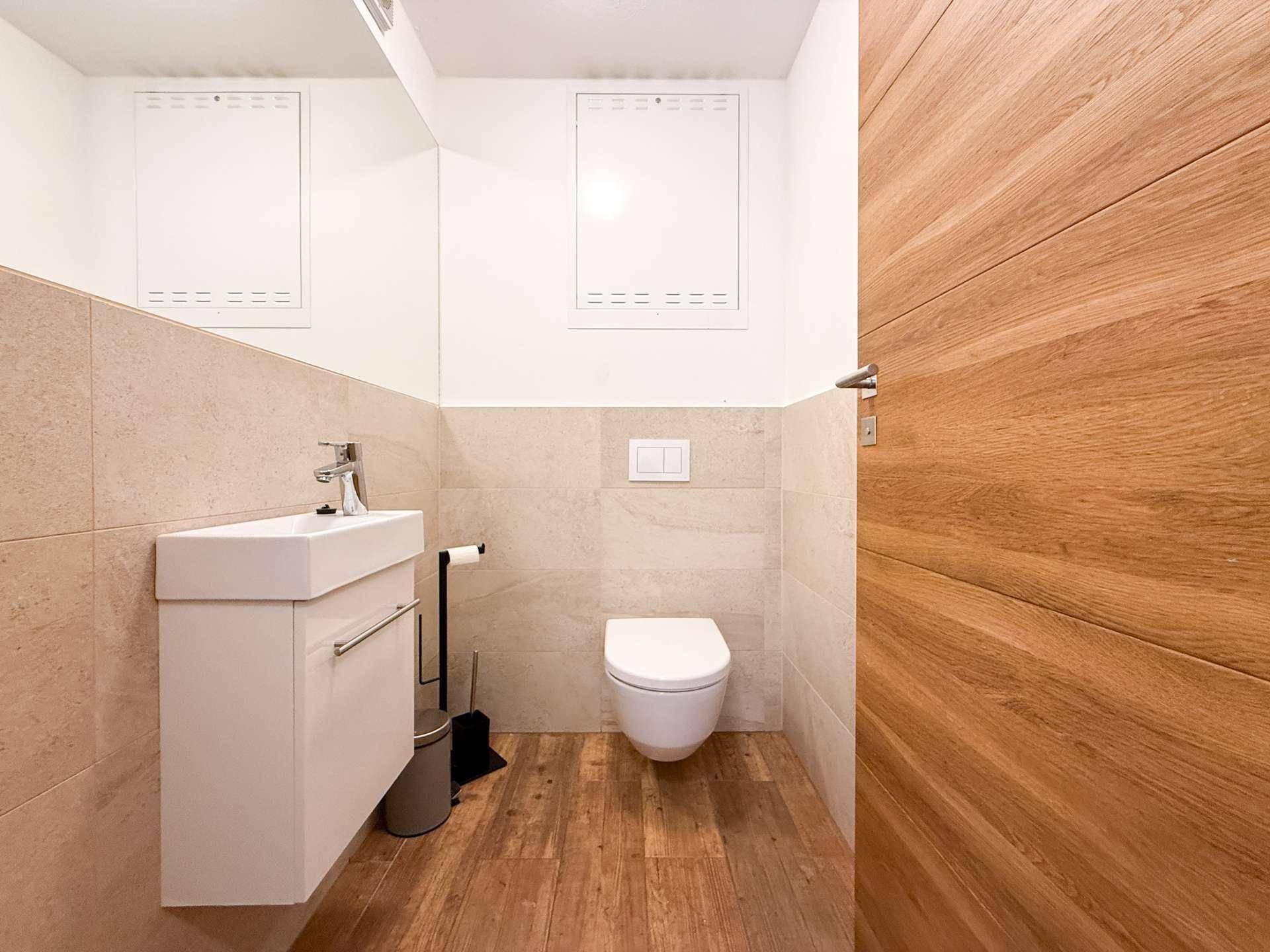 Modernes Gäste-WC mit Wand-WC, Waschtisch und einer Kombination aus Fliesen- und Holzboden.