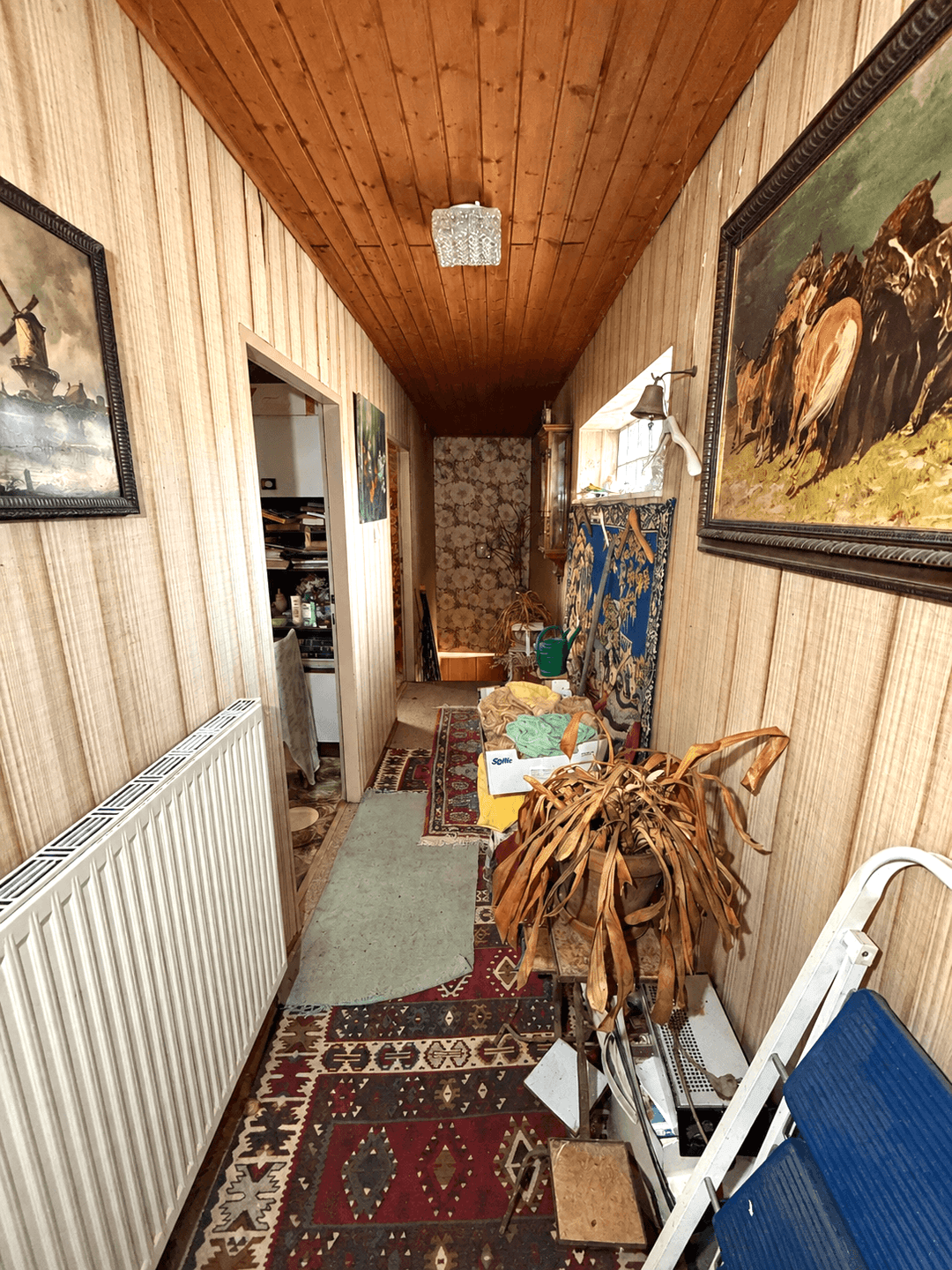Schmaler Flur mit Holzdecke und Teppichboden, viele persönliche Gegenstände.