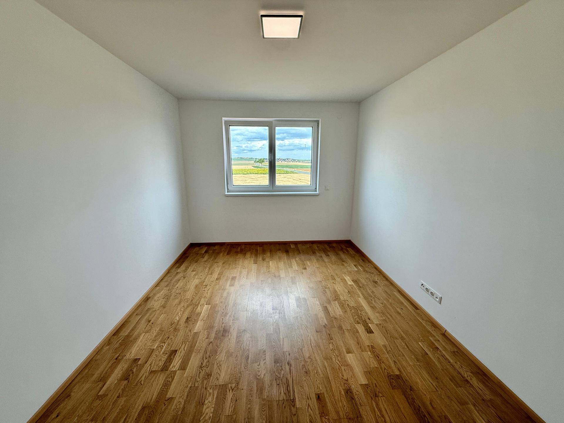 Helles Schlafzimmer mit Holzboden und Fenster, das einen weiten Blick in die Natur ermöglicht.
