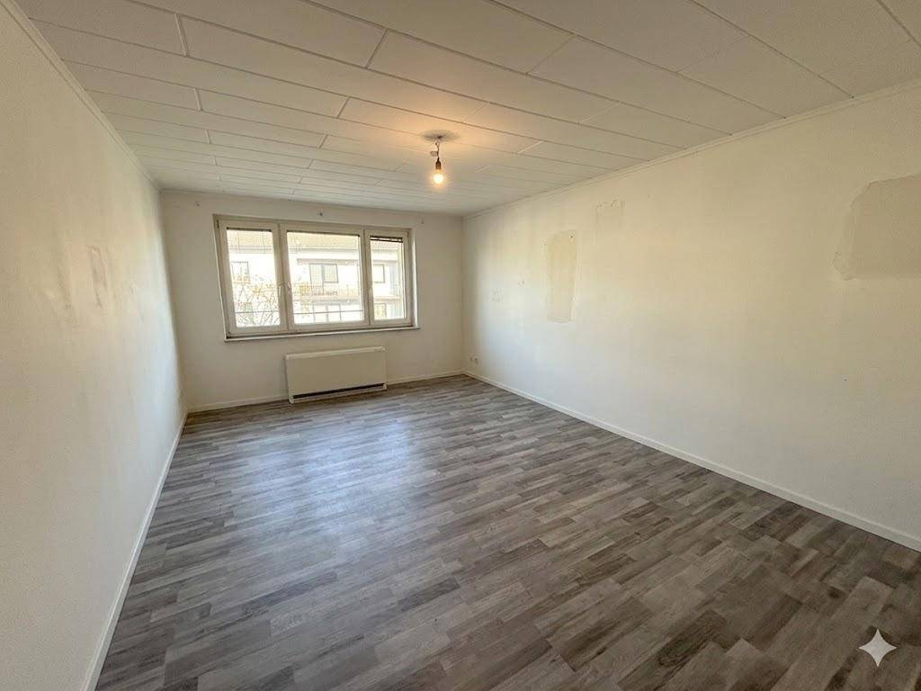 Geräumiges, unmöbliertes Zimmer mit Laminatboden und Blick auf die Umgebung durch das Fenster.