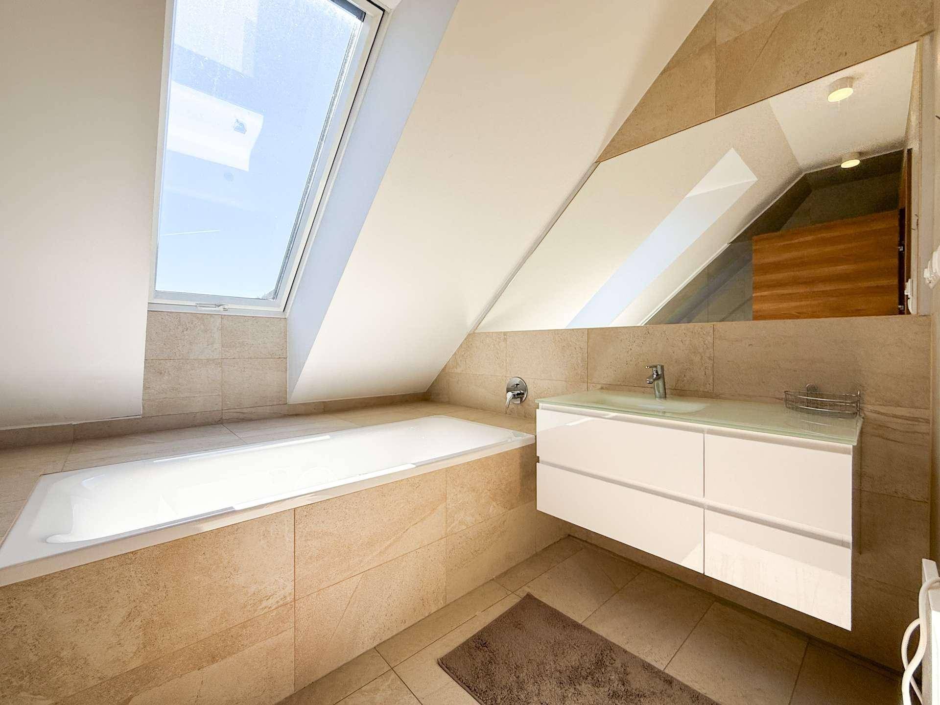 Geräumiges Badezimmer mit Badewanne, Waschtisch, großem Spiegel und einem Dachfenster für natürliches Licht.