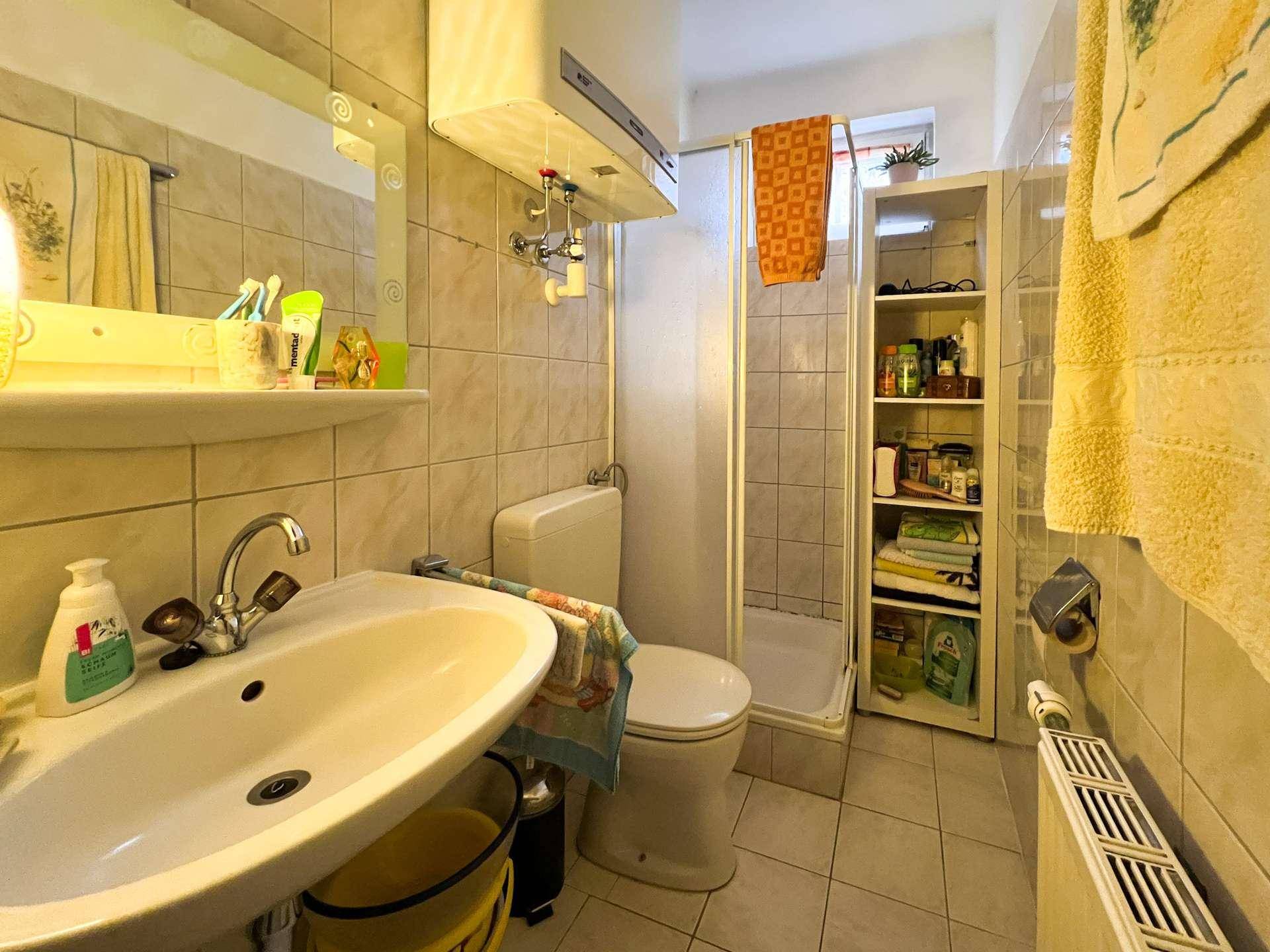 Gefliestes Badezimmer mit Waschbecken, Toilette und Duschkabine, ausgestattet mit einem Fenster.