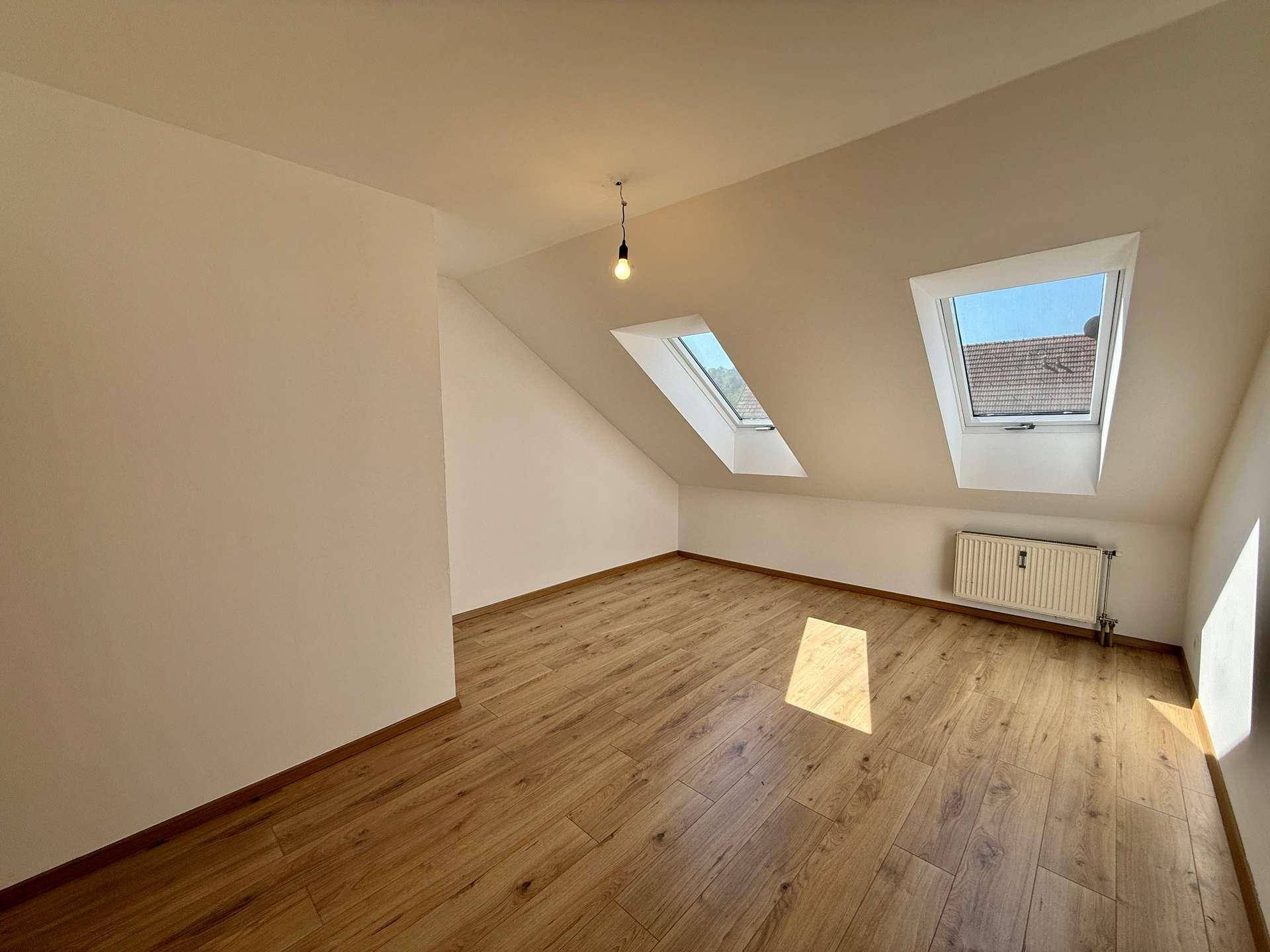 Geräumiges Dachzimmer mit Laminatboden und viel Tageslicht durch die Dachfenster.