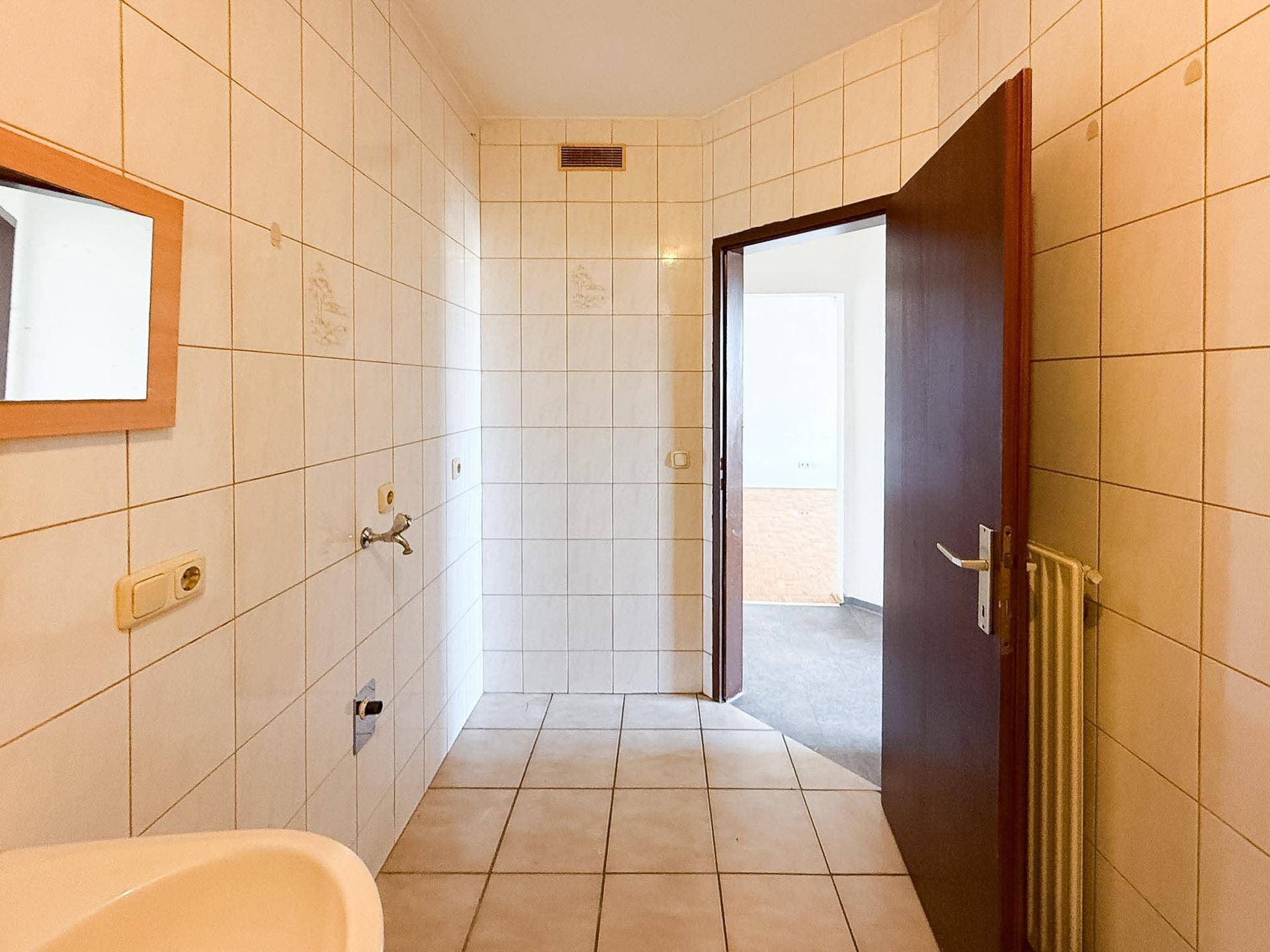 Gefliestes Badezimmer mit Waschbecken und Zugang zu einem weiteren Raum, möglicherweise einem WC.