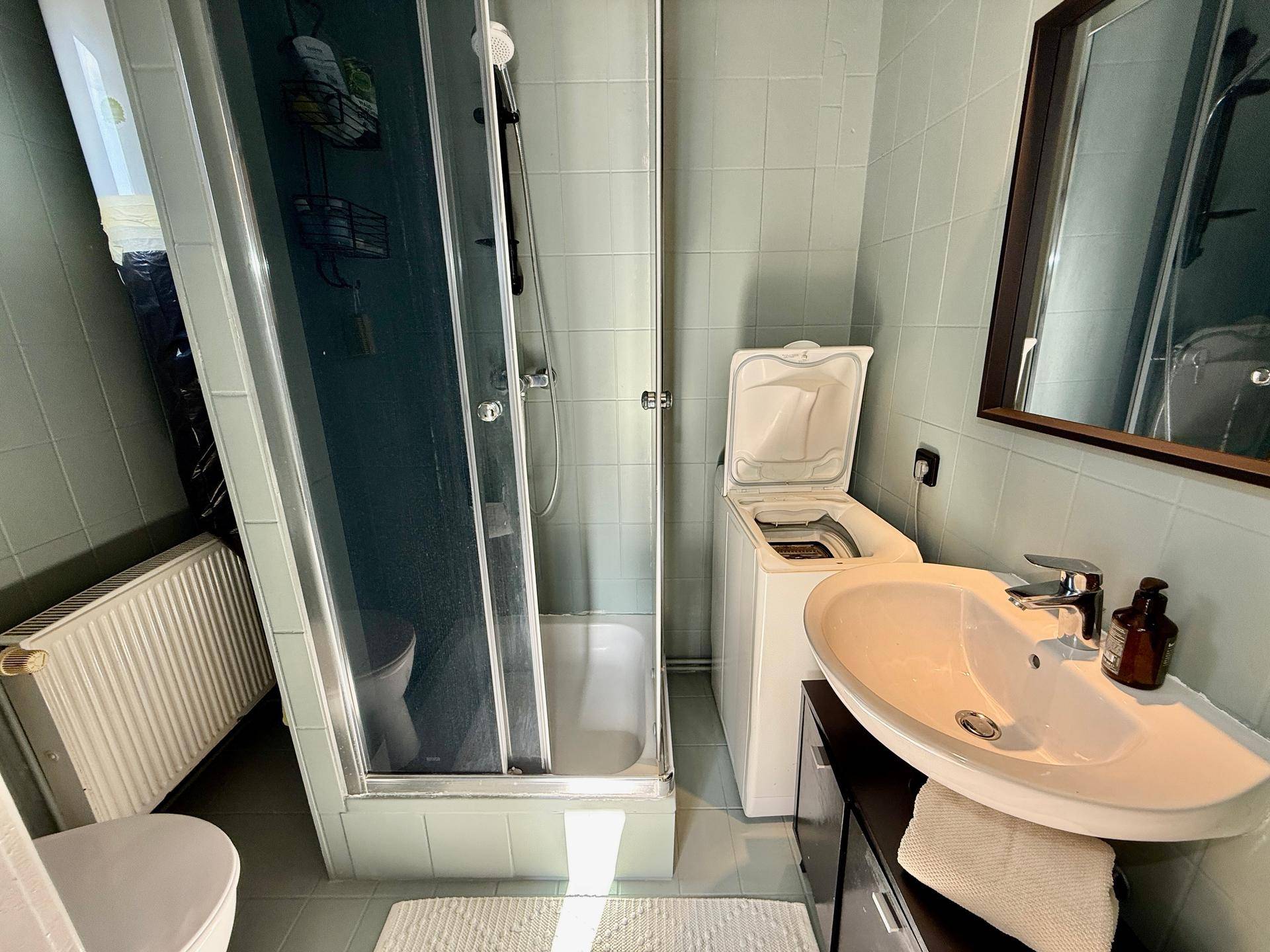 Badezimmer mit Duschkabine, Waschbecken und Waschmaschine, ausgestattet mit hellblauen Fliesen.