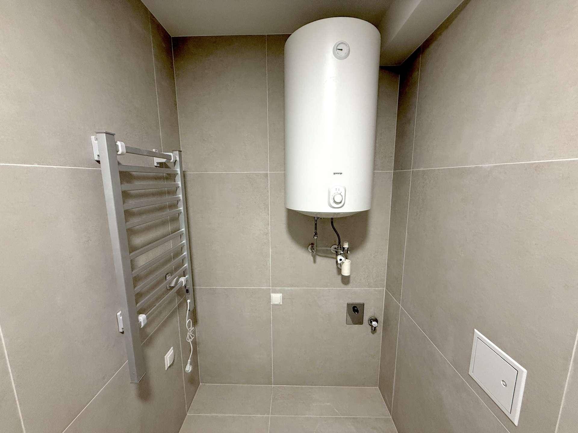 Badezimmerbereich mit Warmwasserboiler und einem praktischen beheizbaren Handtuchhalter an der Wand.