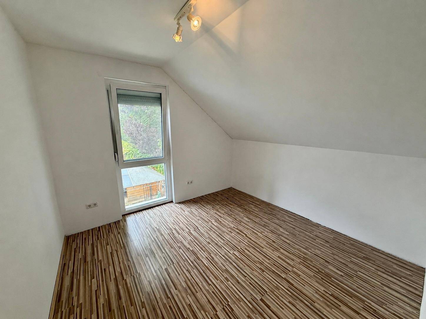 Gemütliches Zimmer unter der Dachschräge mit Laminatboden und einem Fenster.