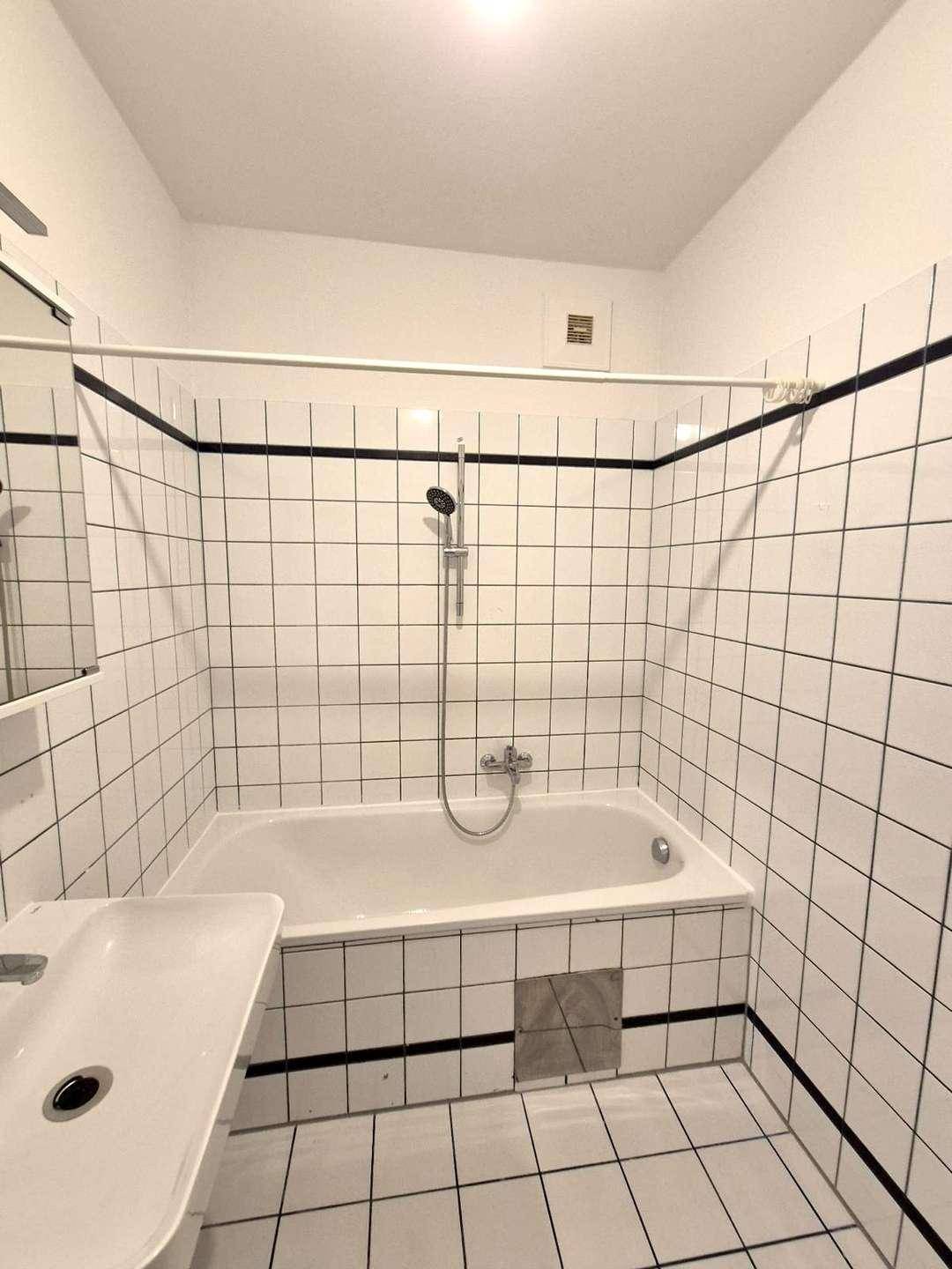 Badezimmer mit Badewanne, Waschbecken und weißen Fliesen, klassisch und funktional gestaltet.