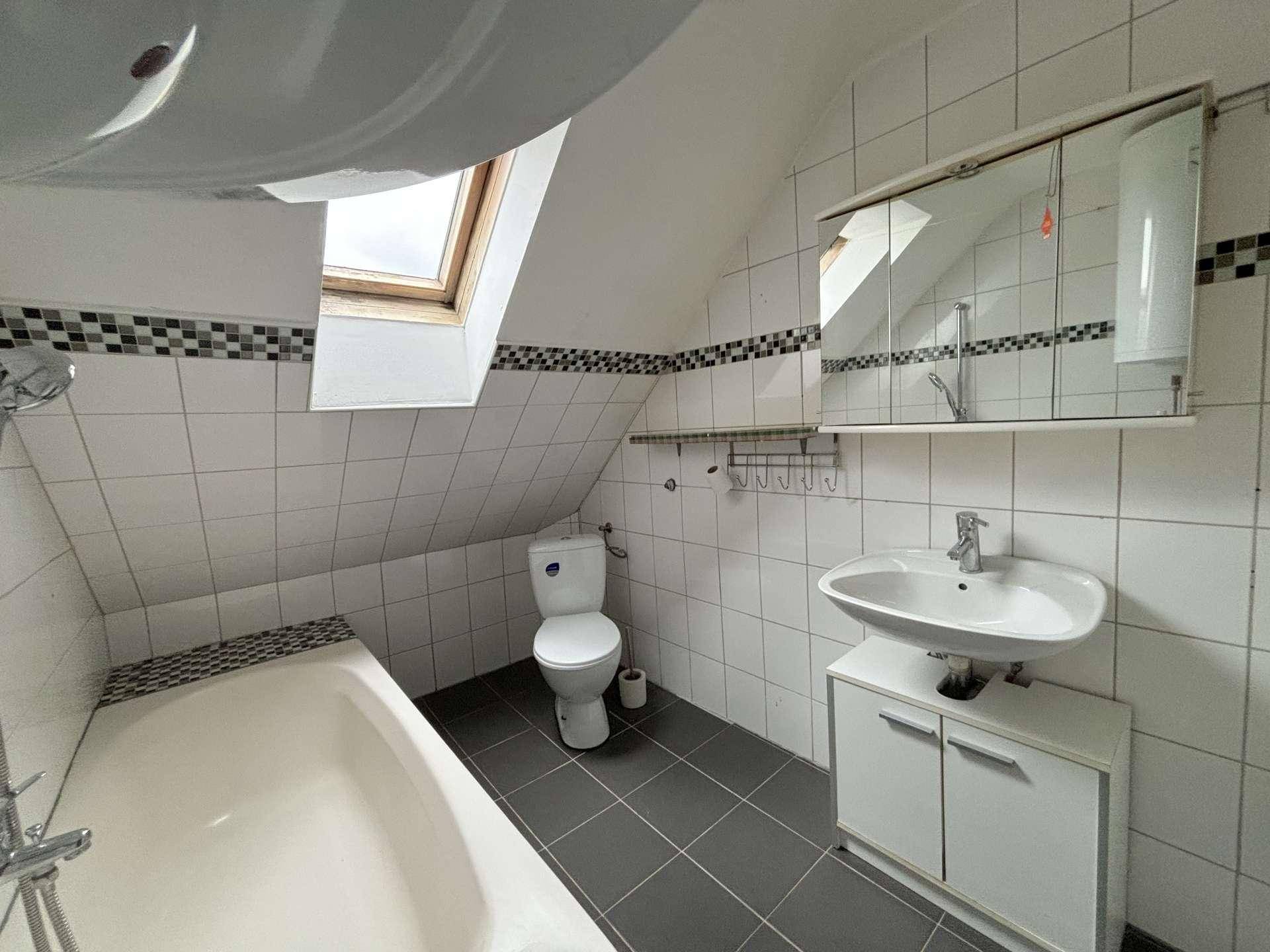 Badezimmer mit Badewanne, WC und Waschbecken, ausgestattet mit Dachfenster.