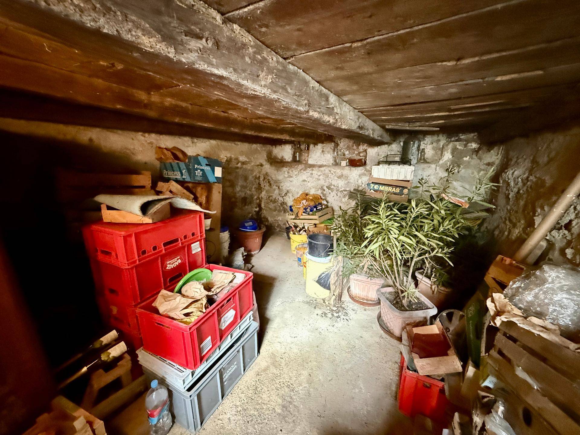 Lagerraum mit freiliegenden Holzbalken, rauen Wänden und verschiedenen gelagerten Gegenständen.