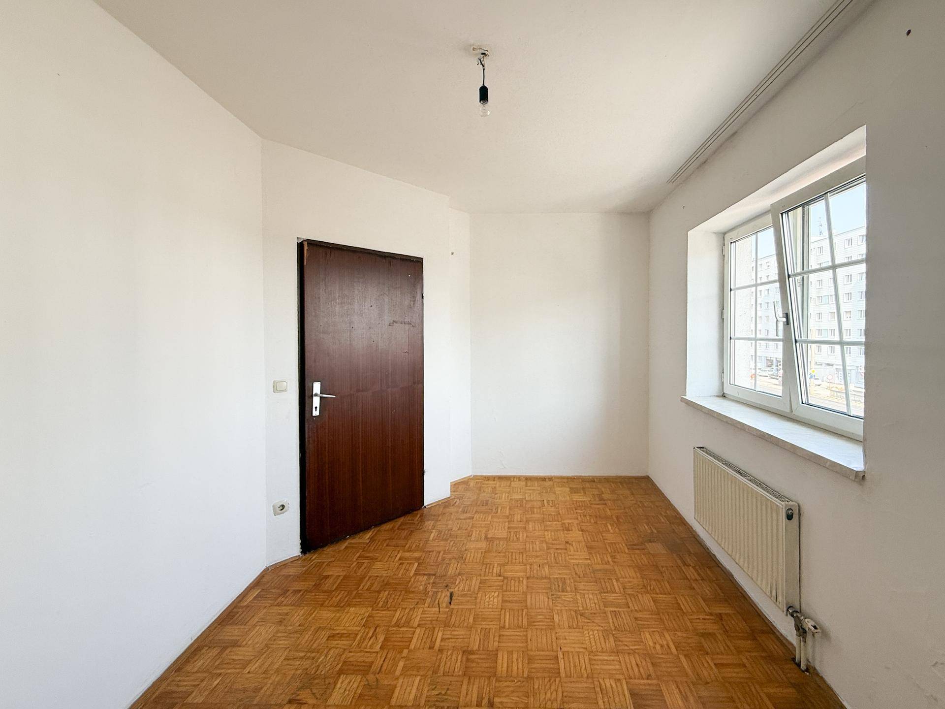 Geräumiges Zimmer mit Parkettboden und Fenster, das eine angenehme Helligkeit bietet.