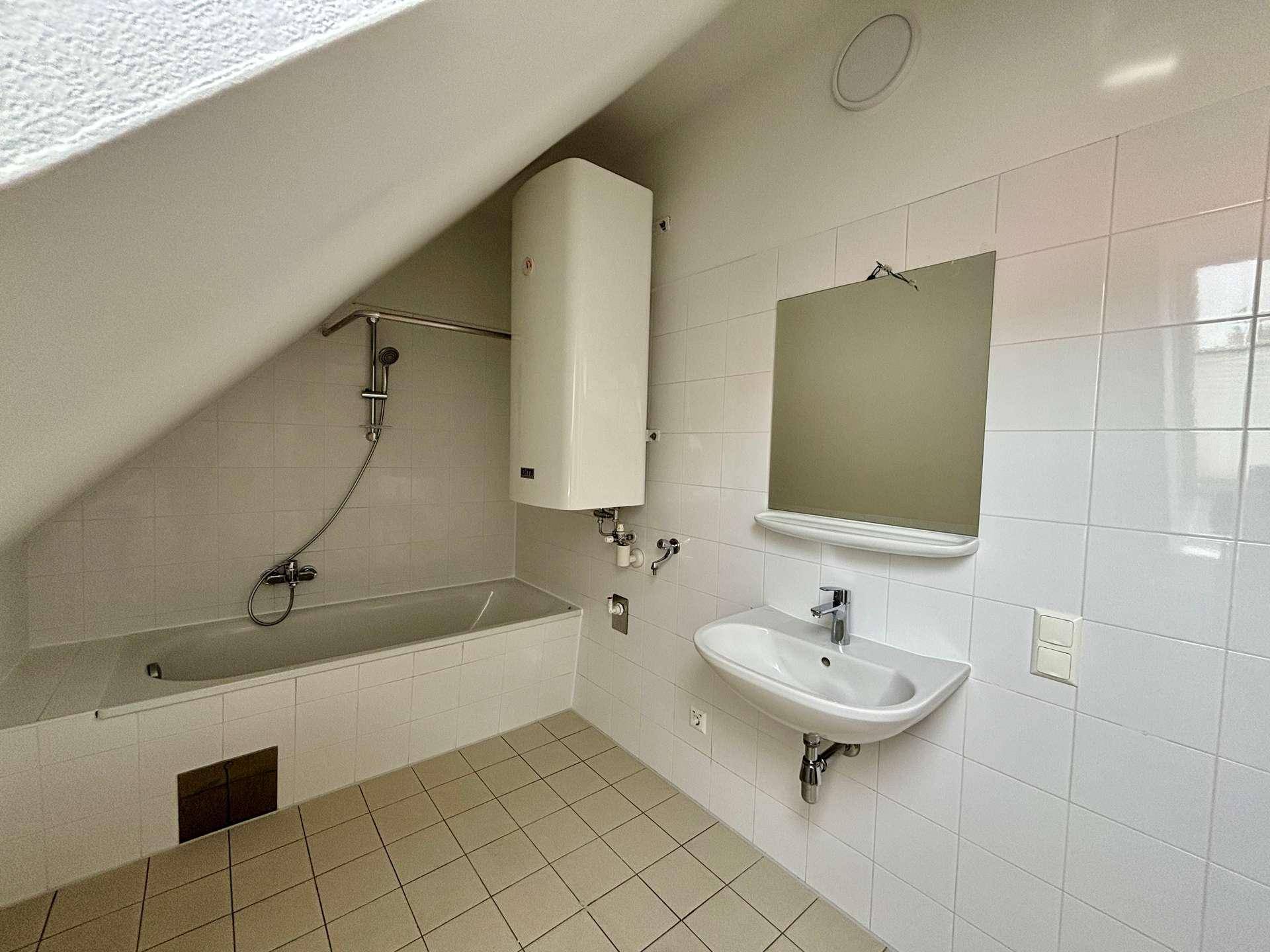 Helles Badezimmer mit weißen Fliesen, Badewanne mit Duschfunktion und modernem Waschbecken.