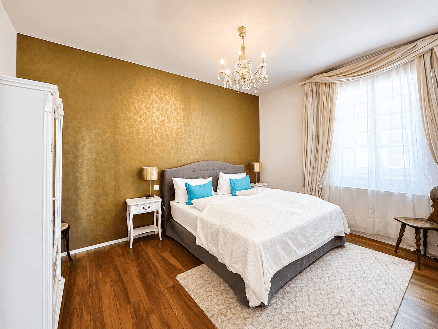 Elegantes Schlafzimmer mit Doppelbett, goldener Akzentwand und Kronleuchter.